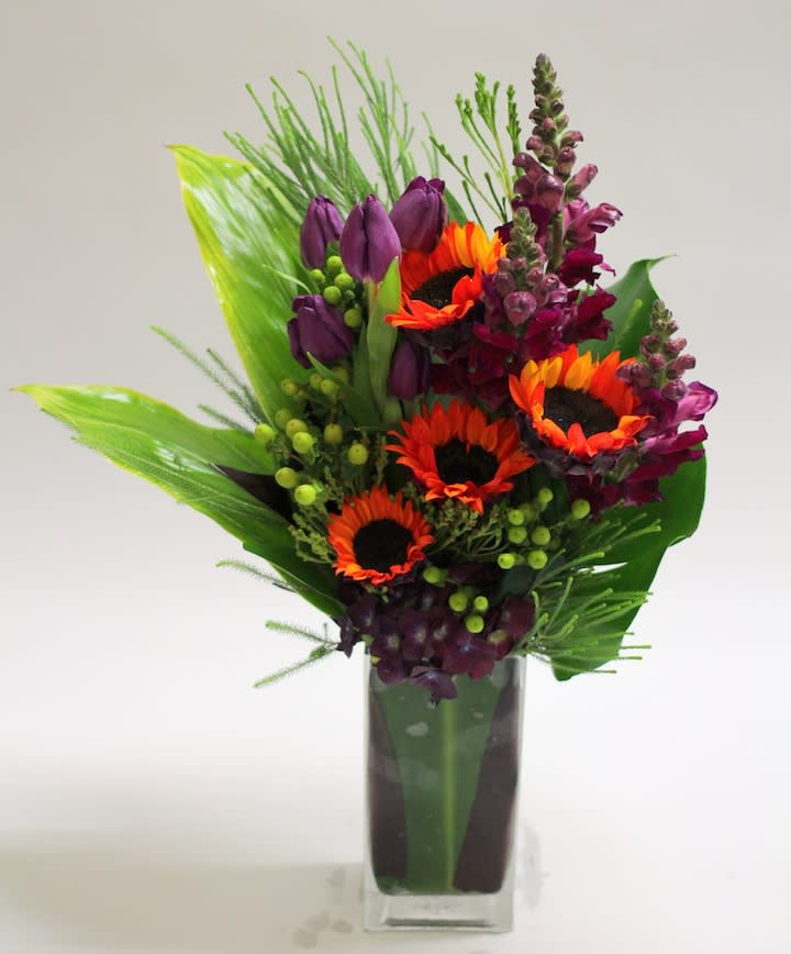 Bright bouquet of orange sunflowers and purple blooms in a clear glass vase
