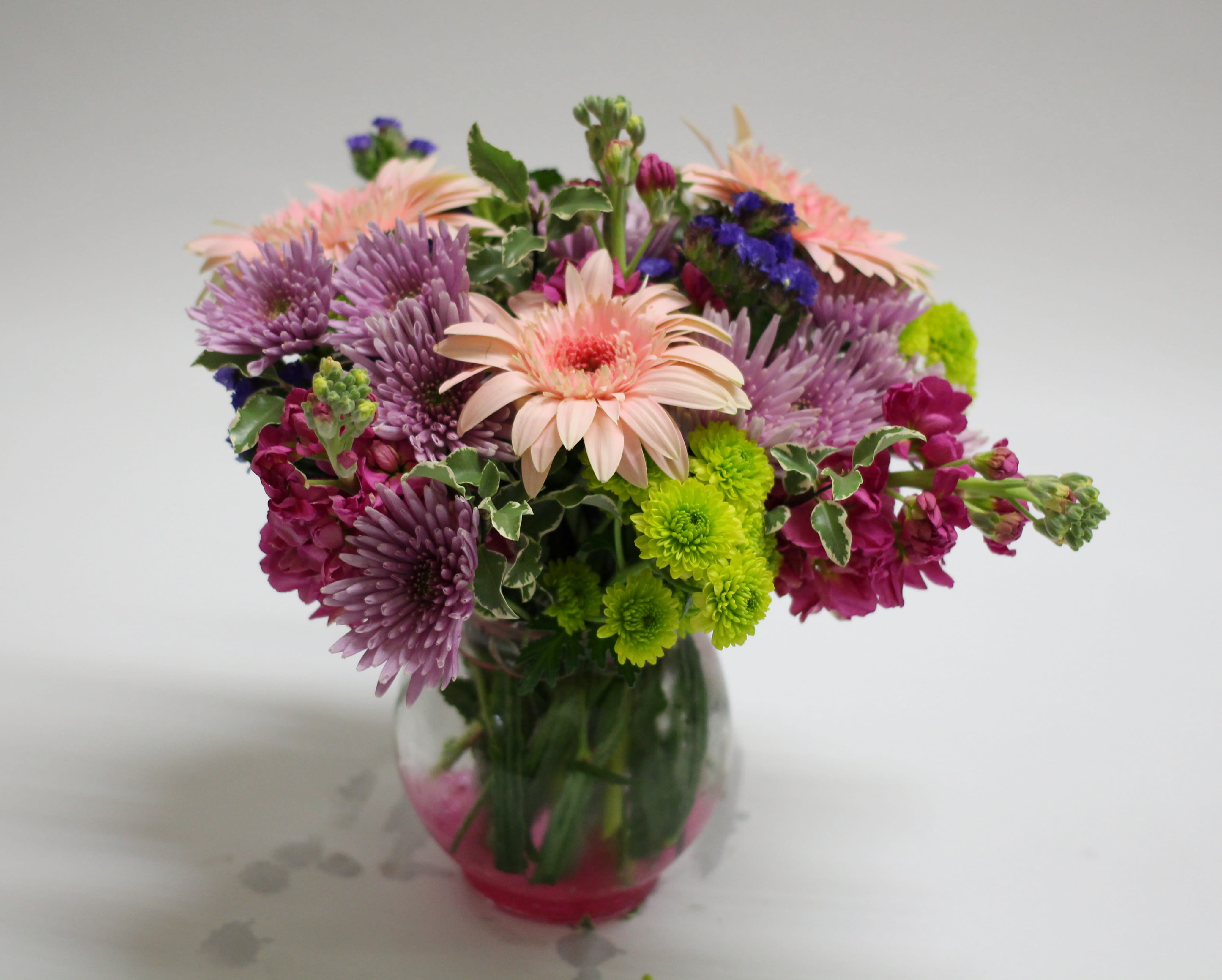 Mixed bouquet of pink, purple, and green flowers in a glass vase