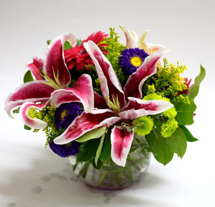 Bouquet of pink-and-white lilies with purple and yellow flowers in a glass vase