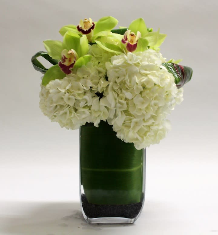 White hydrangeas and green orchids in a tall glass vase