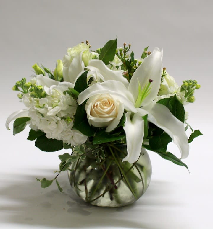 White lilies and a cream rose in a glass vase