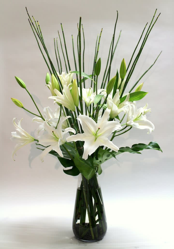 White lilies arranged in a tall glass vase with bamboo stems
