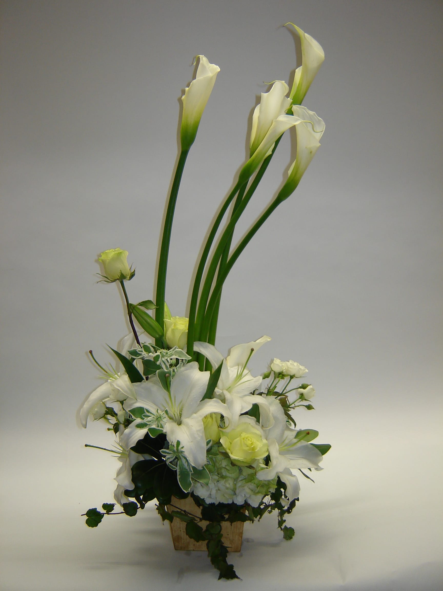 White calla lilies and lilies arranged in a wooden container