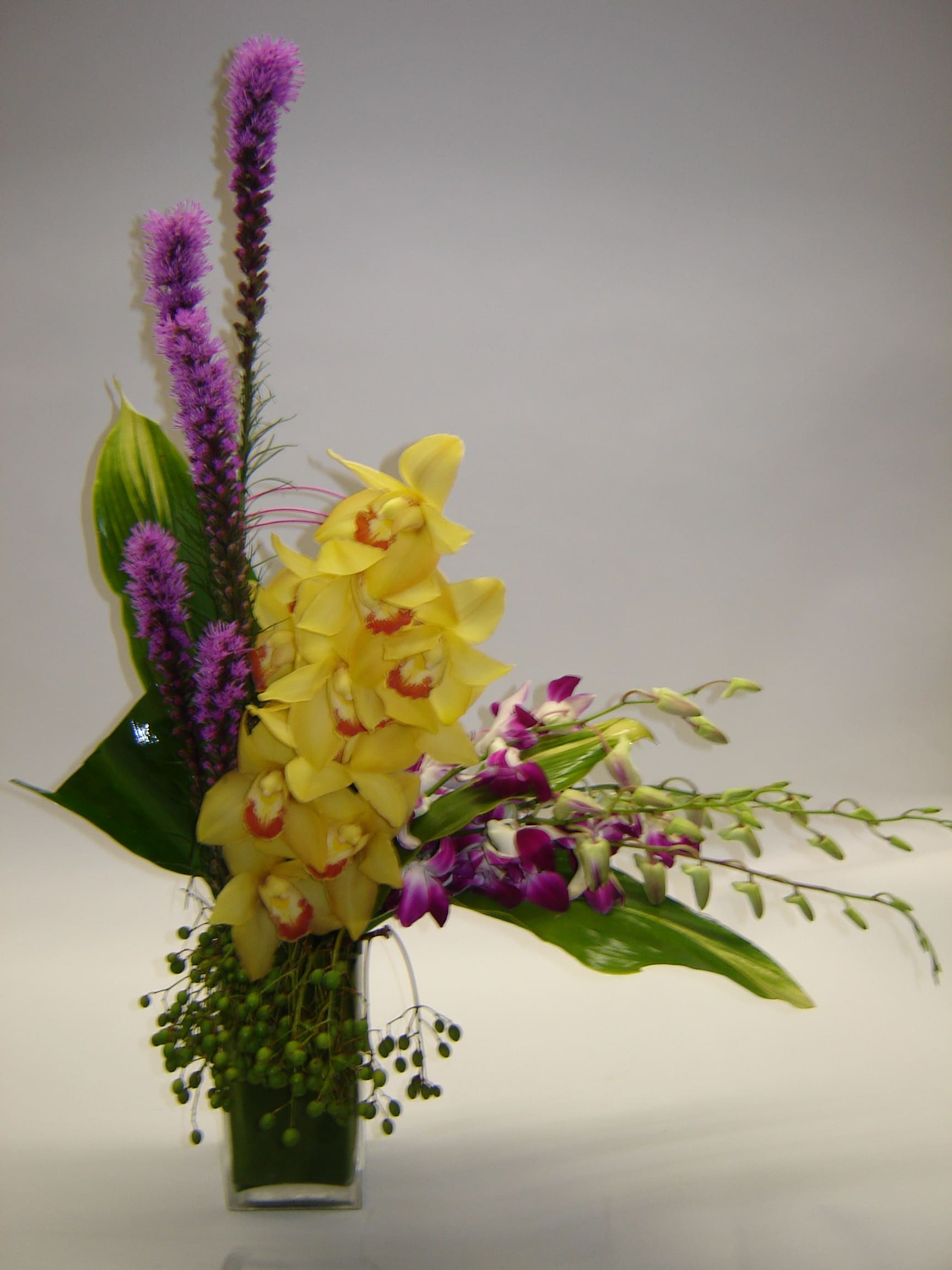 Yellow orchids and purple flowers in a clear glass vase