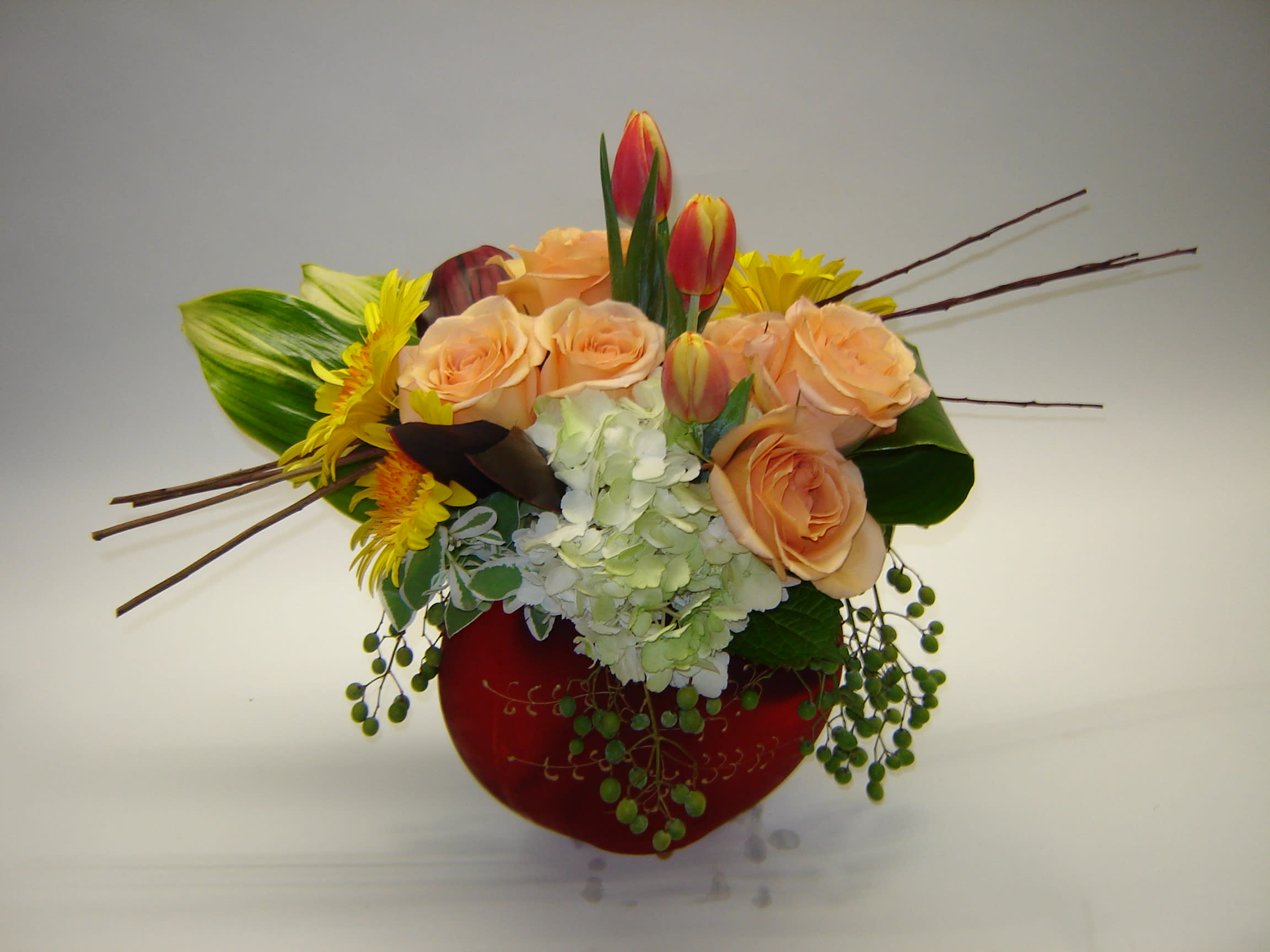 Peach roses and yellow flowers in a red vase