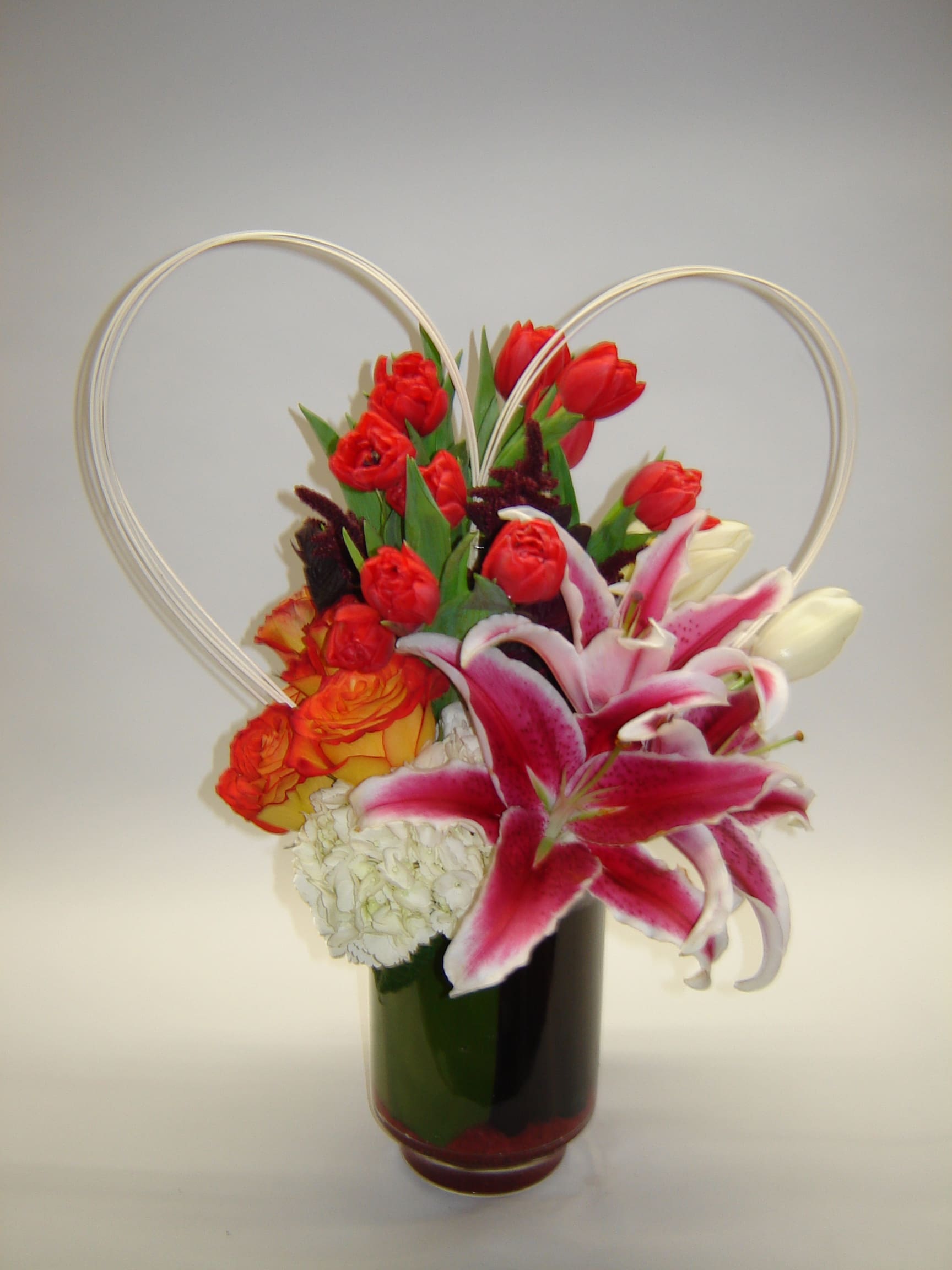Red tulips and pink lilies in a dark vase with heart-shaped wire handles