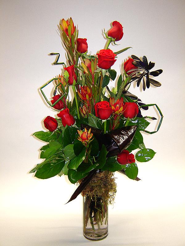 Tall bouquet of red roses and tropical flowers in a glass vase