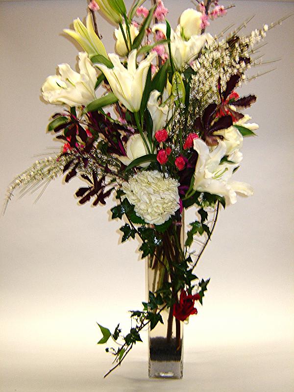 Tall bouquet of white lilies and mixed flowers in a clear glass vase