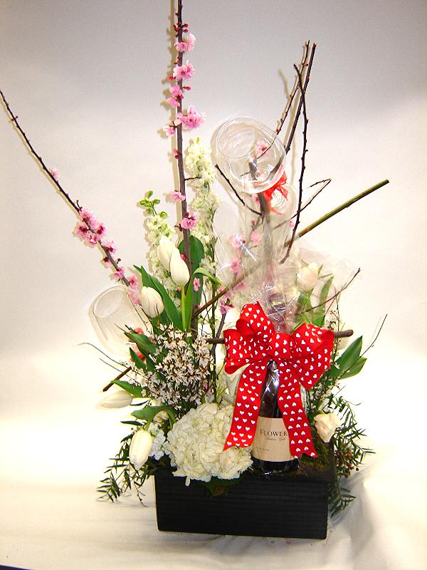 Tall floral gift arrangement with white blooms, pink blossoms, and a red bow on a bottle