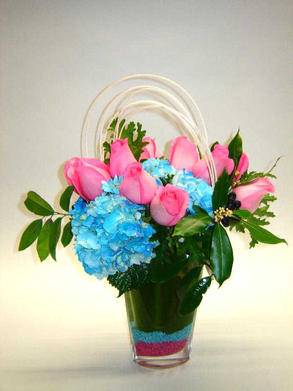 Pink roses and blue hydrangeas in a clear vase with arched handles