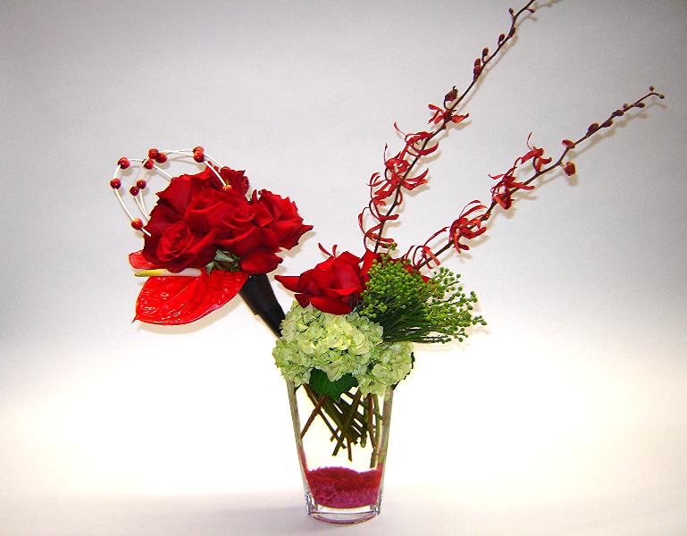 Red roses arranged in a clear glass vase with green hydrangea and decorative branches