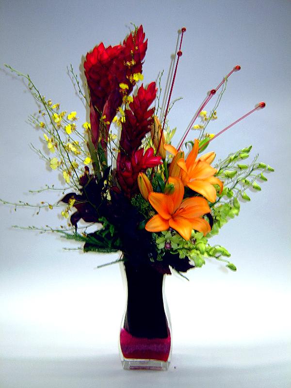 Orange lilies and red tropical flowers in a tall vase