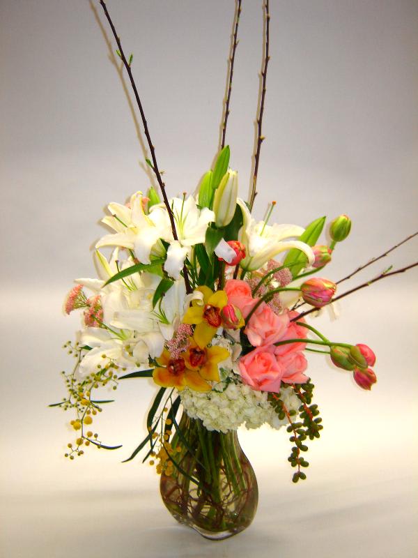 Tall mixed floral arrangement in a glass vase with lilies and pink roses