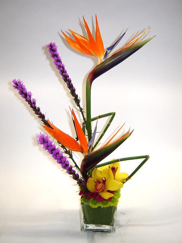 Tropical flower arrangement in a clear glass vase with orange bird of paradise and yellow orchids