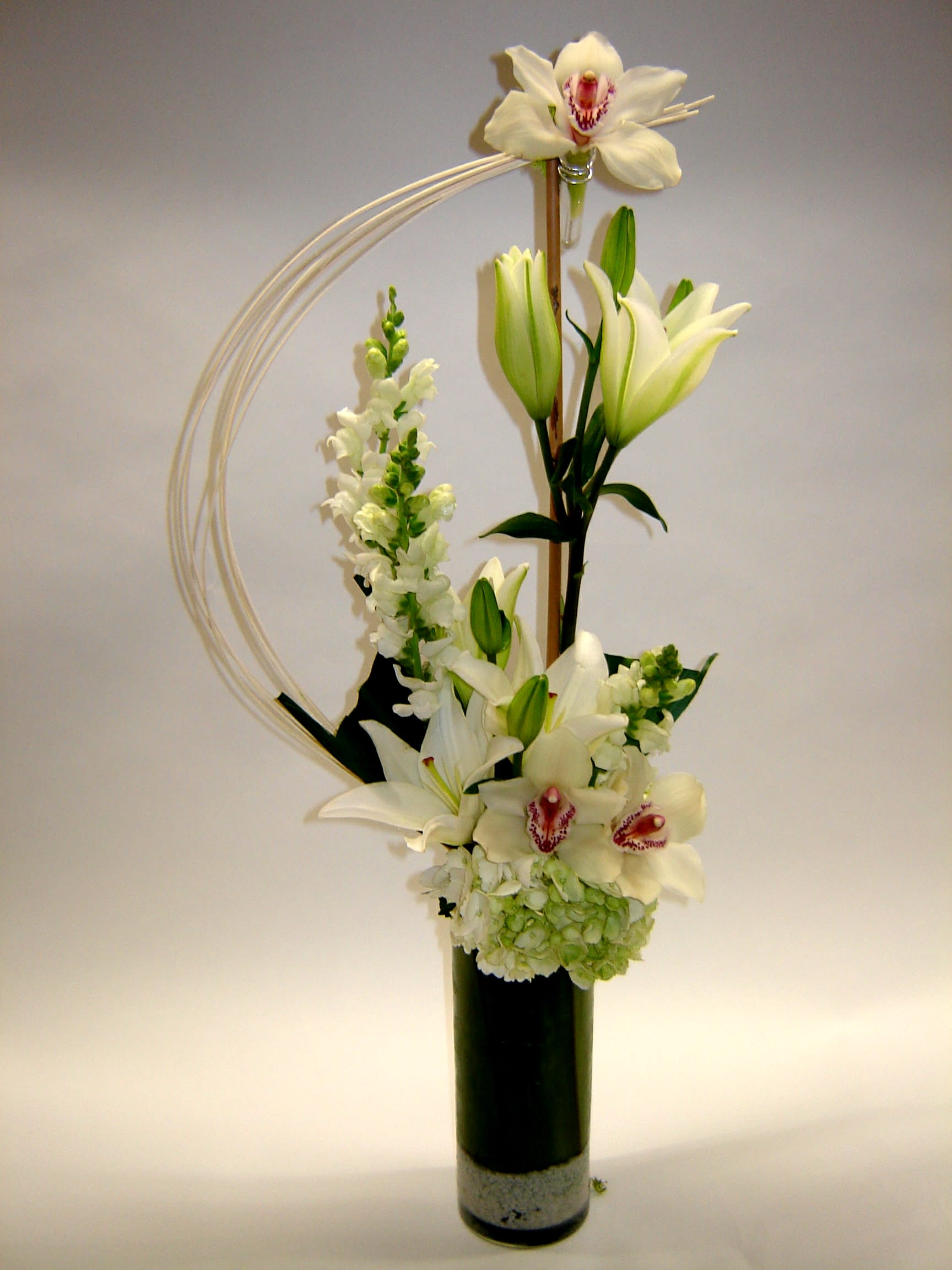 Tall white floral arrangement with lilies and orchids in a black vase