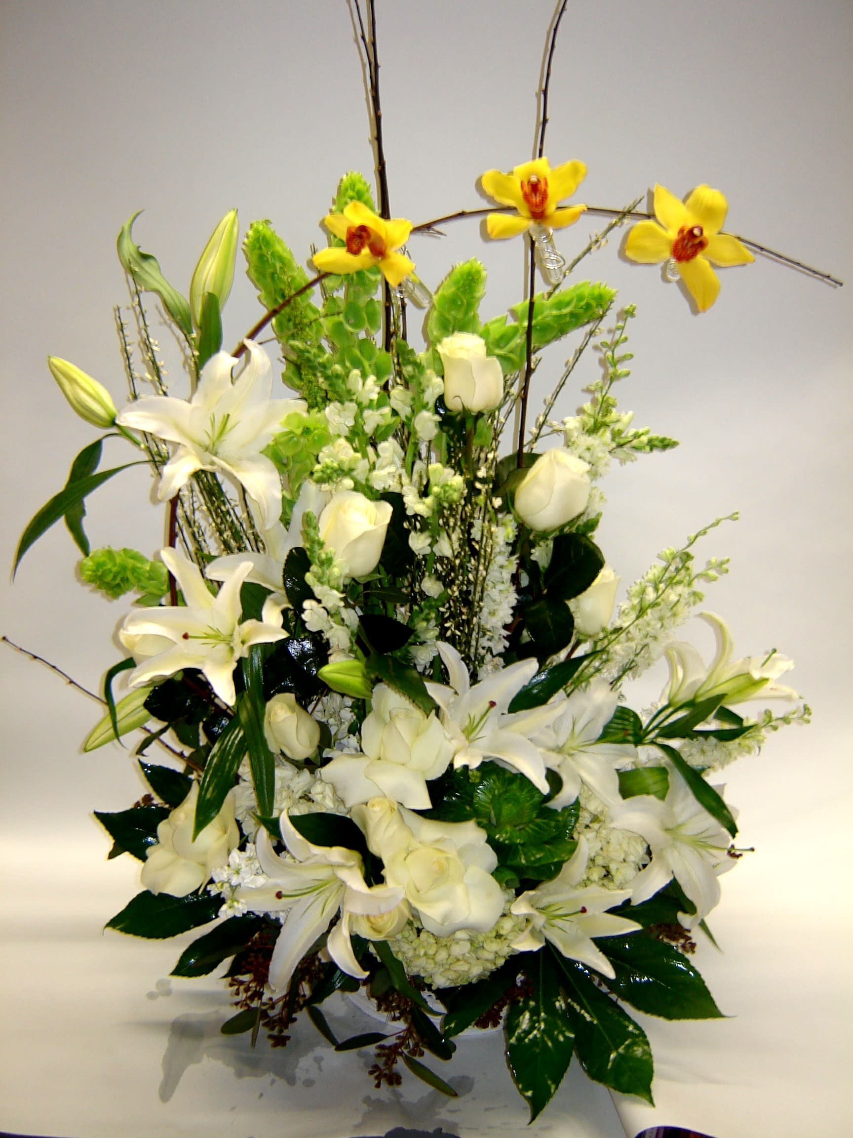 White lilies and roses with yellow orchids in a tall arrangement