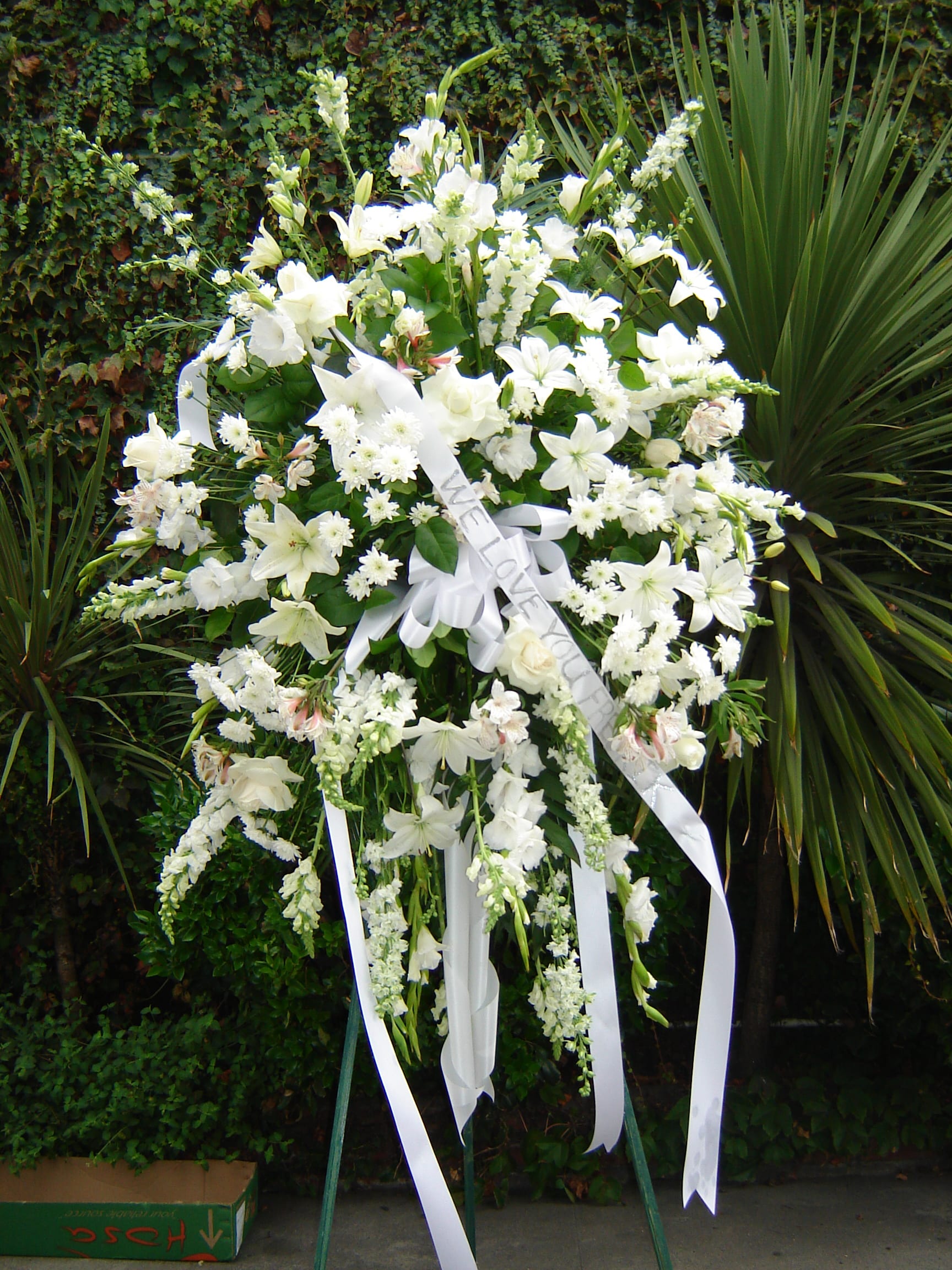 Large white funeral spray on a stand with ribbon streamers