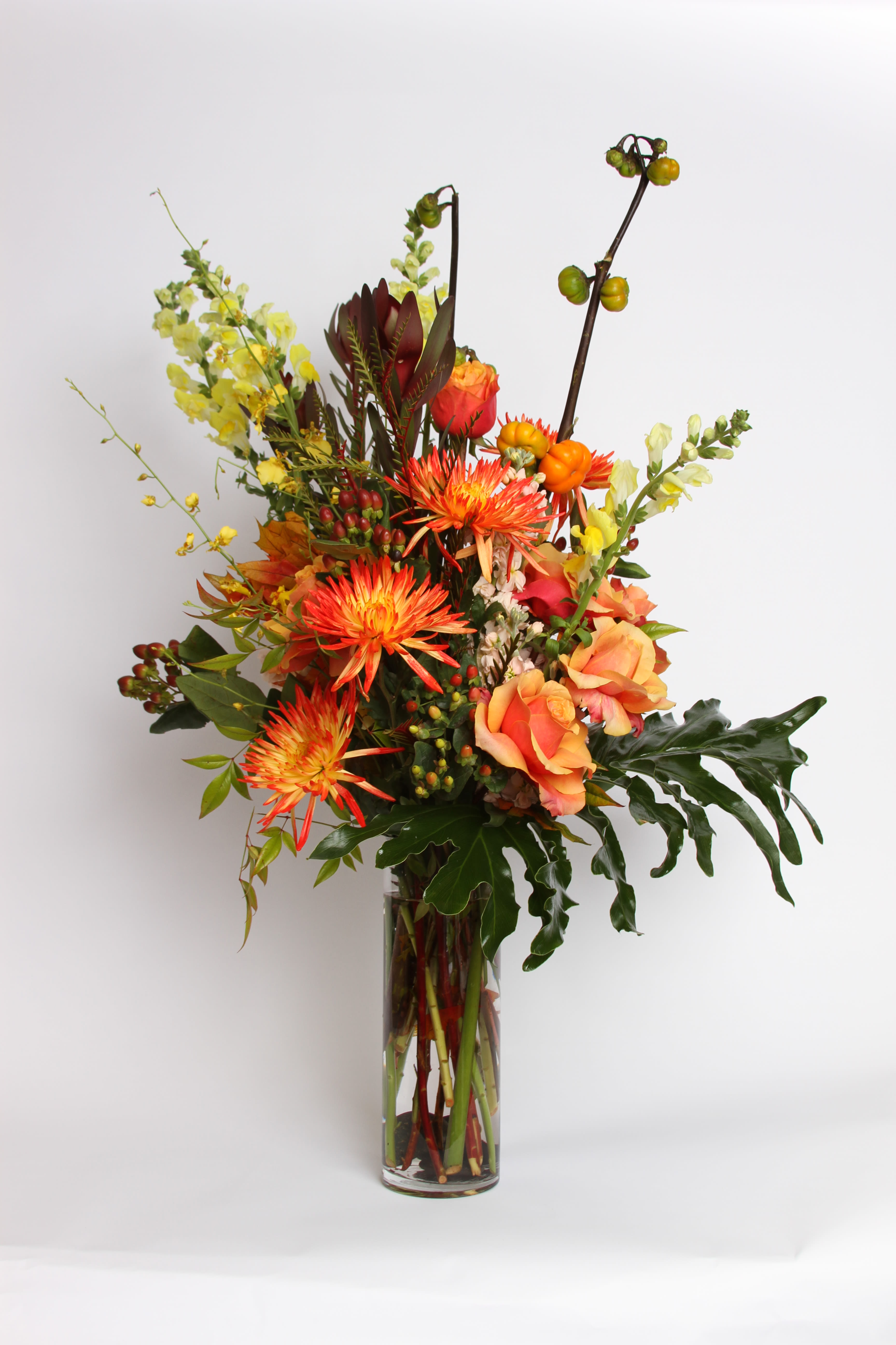 Tall mixed bouquet in a clear glass vase with orange and yellow blooms