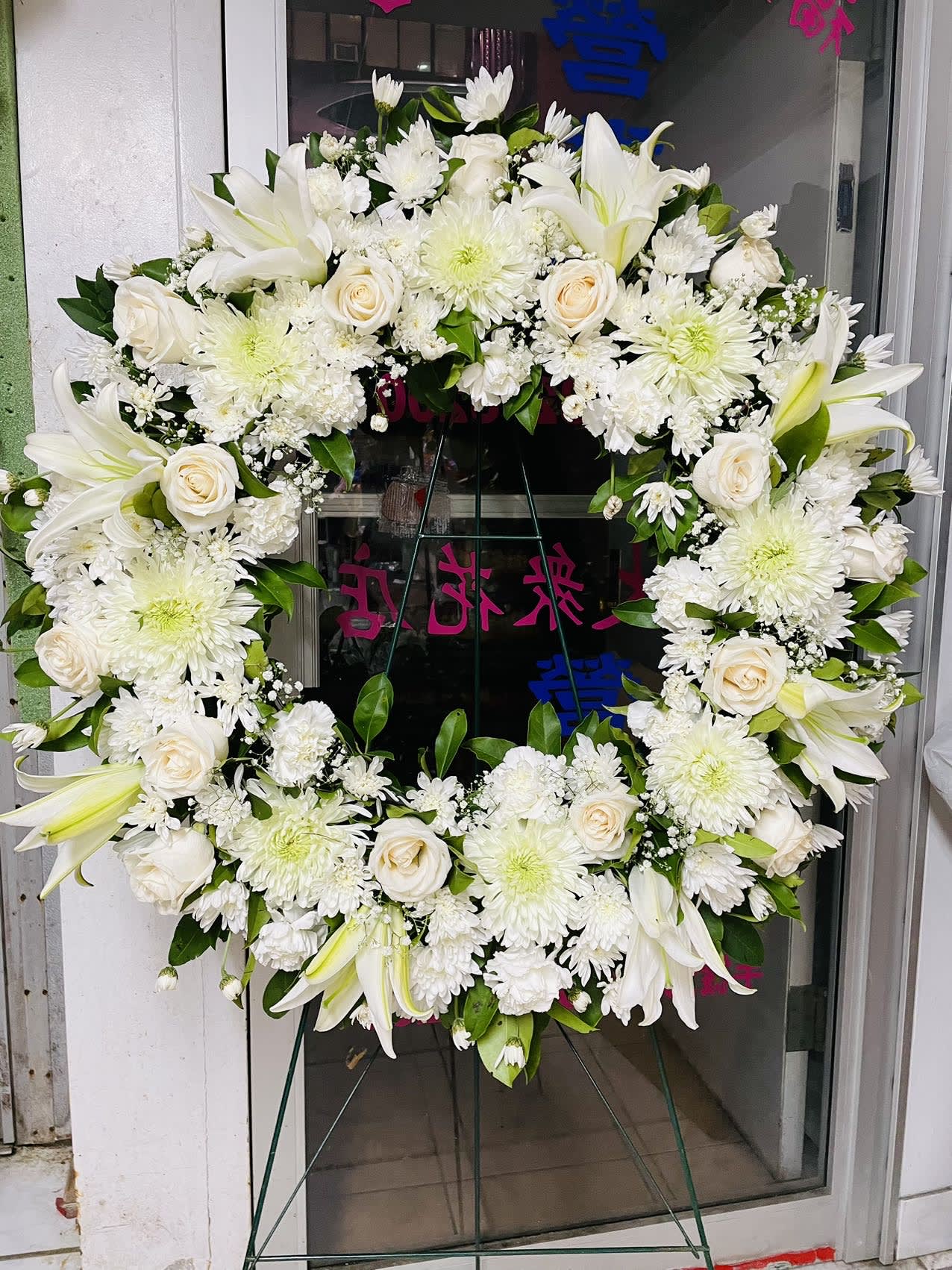 White floral wreath on a stand with roses, lilies, and chrysanthemums