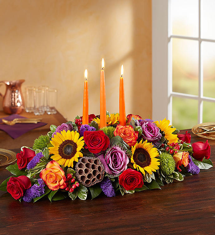 Low floral centerpiece with lit orange candles and mixed roses and sunflowers