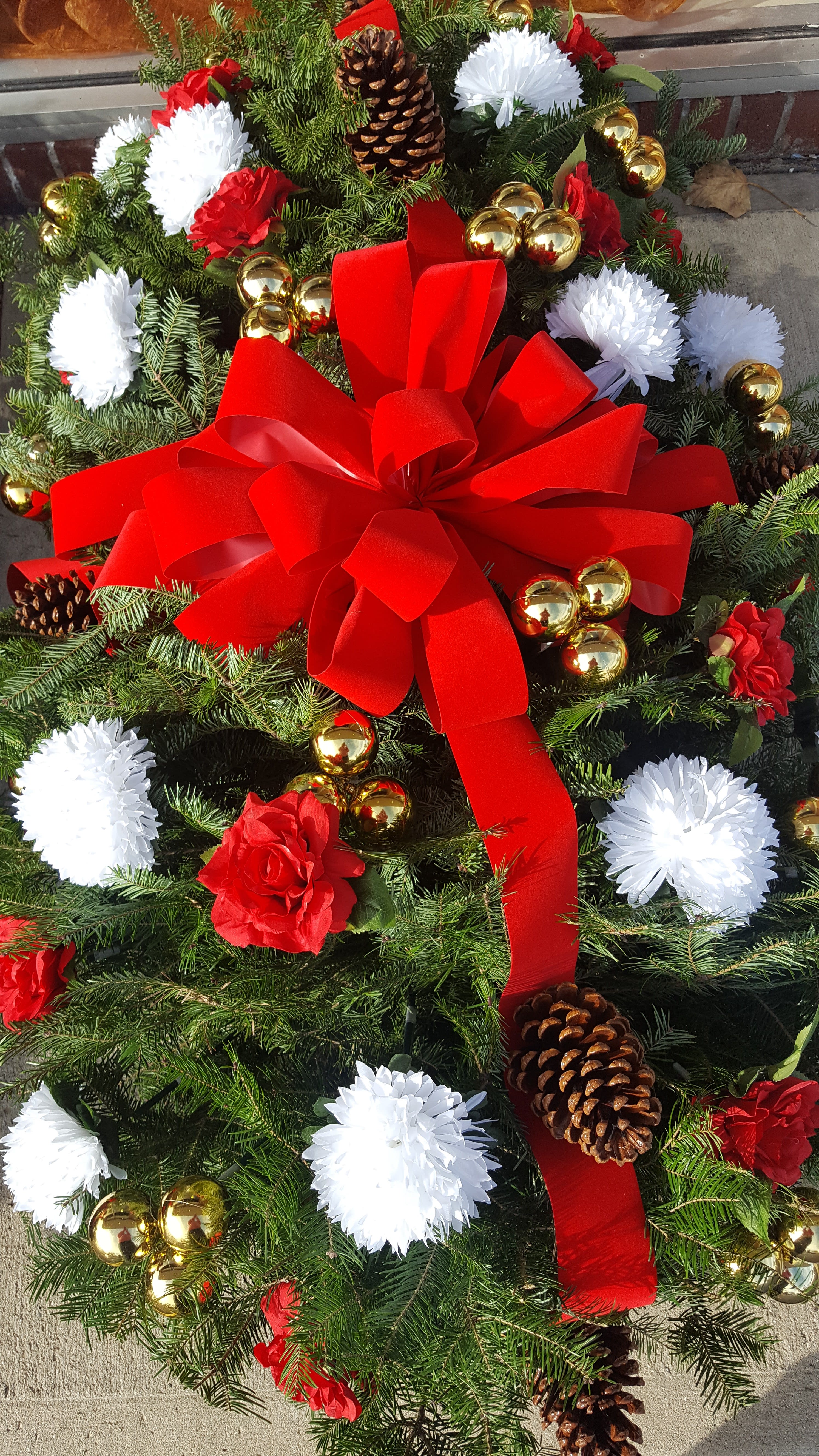 Christmas wreath with red bow, white flowers, pinecones, and gold ornaments