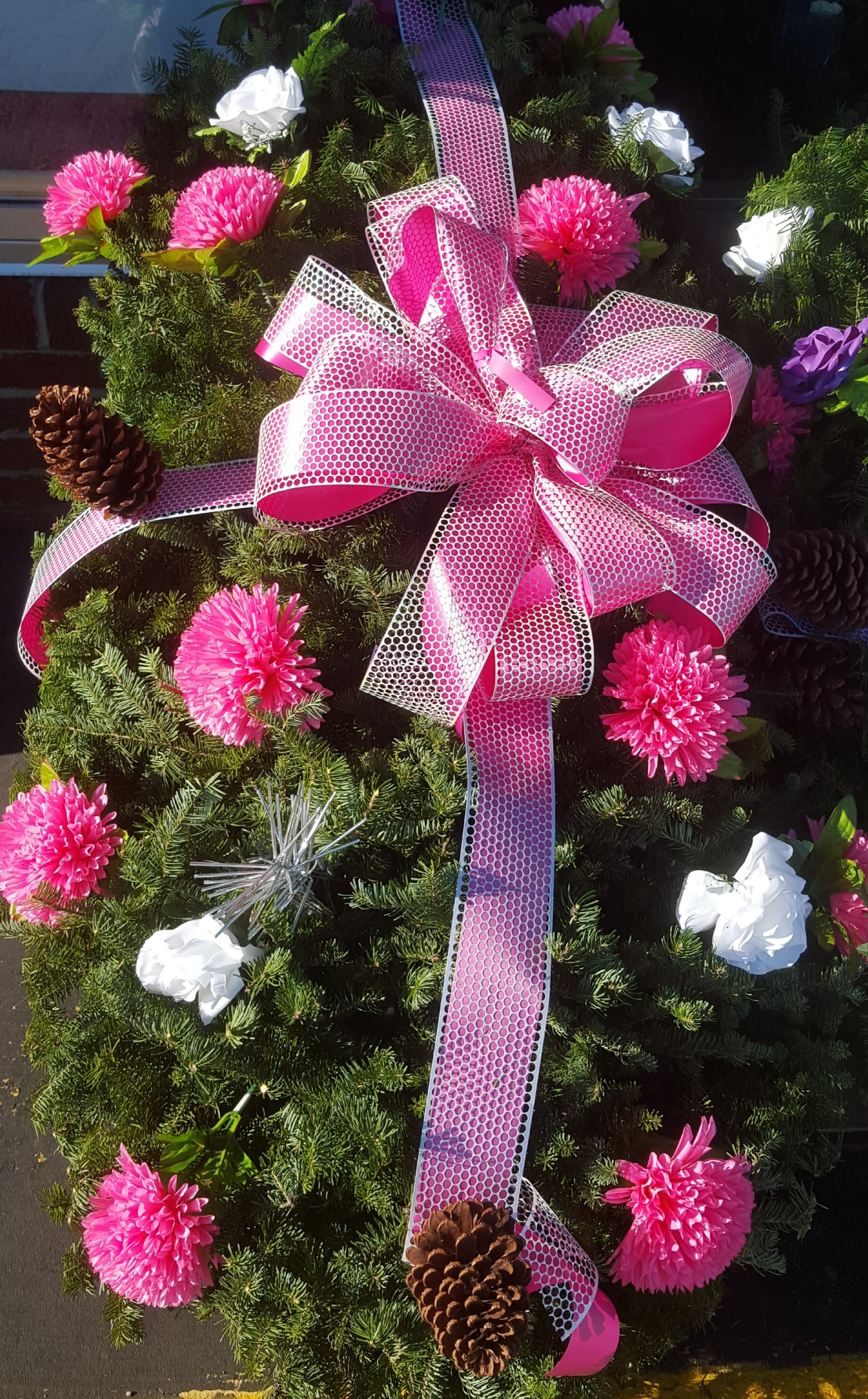 Evergreen wreath with pink ribbon, pink and white flowers, and pinecones