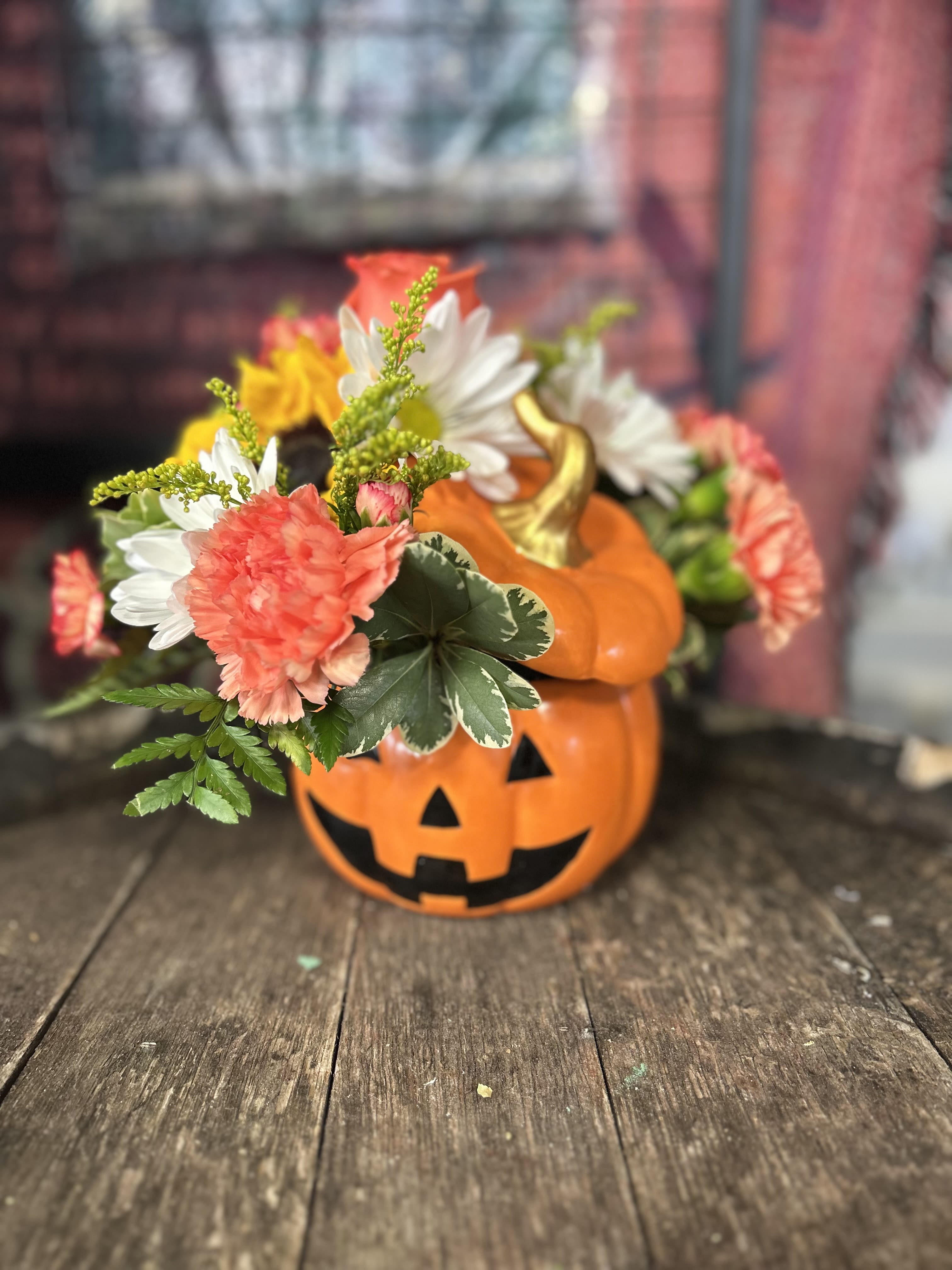 Halloween pumpkin container with mixed flowers and a jack-o'-lantern face