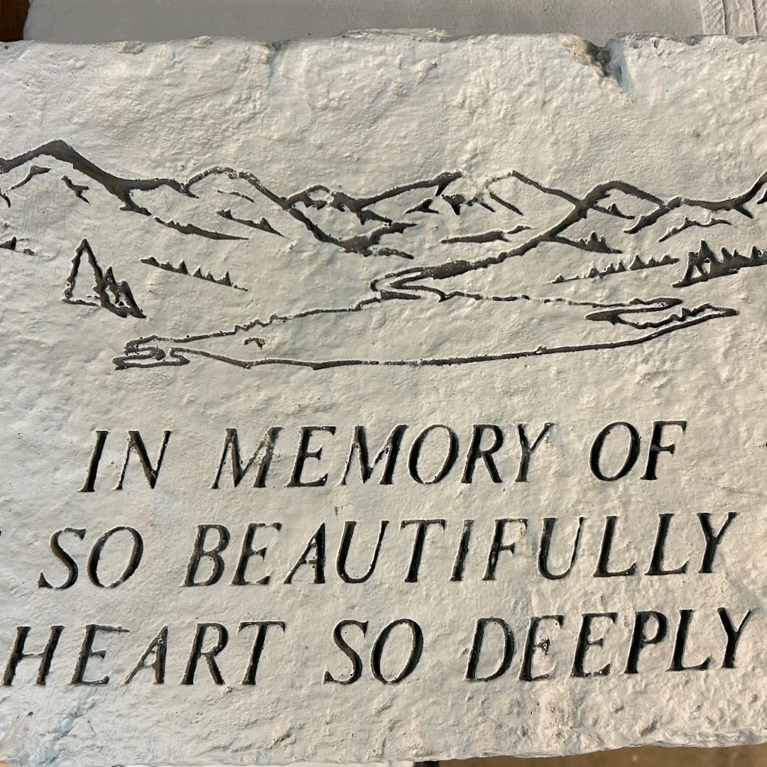 Stone memorial plaque with engraved mountain scene and text
