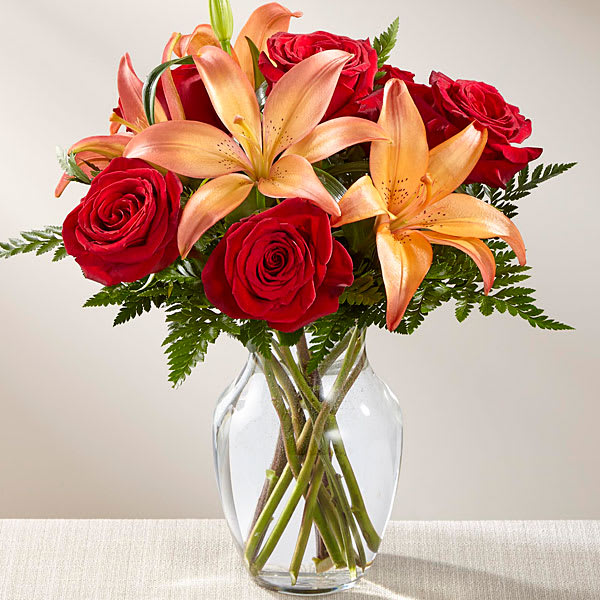 Red roses and peach lilies in a clear glass vase
