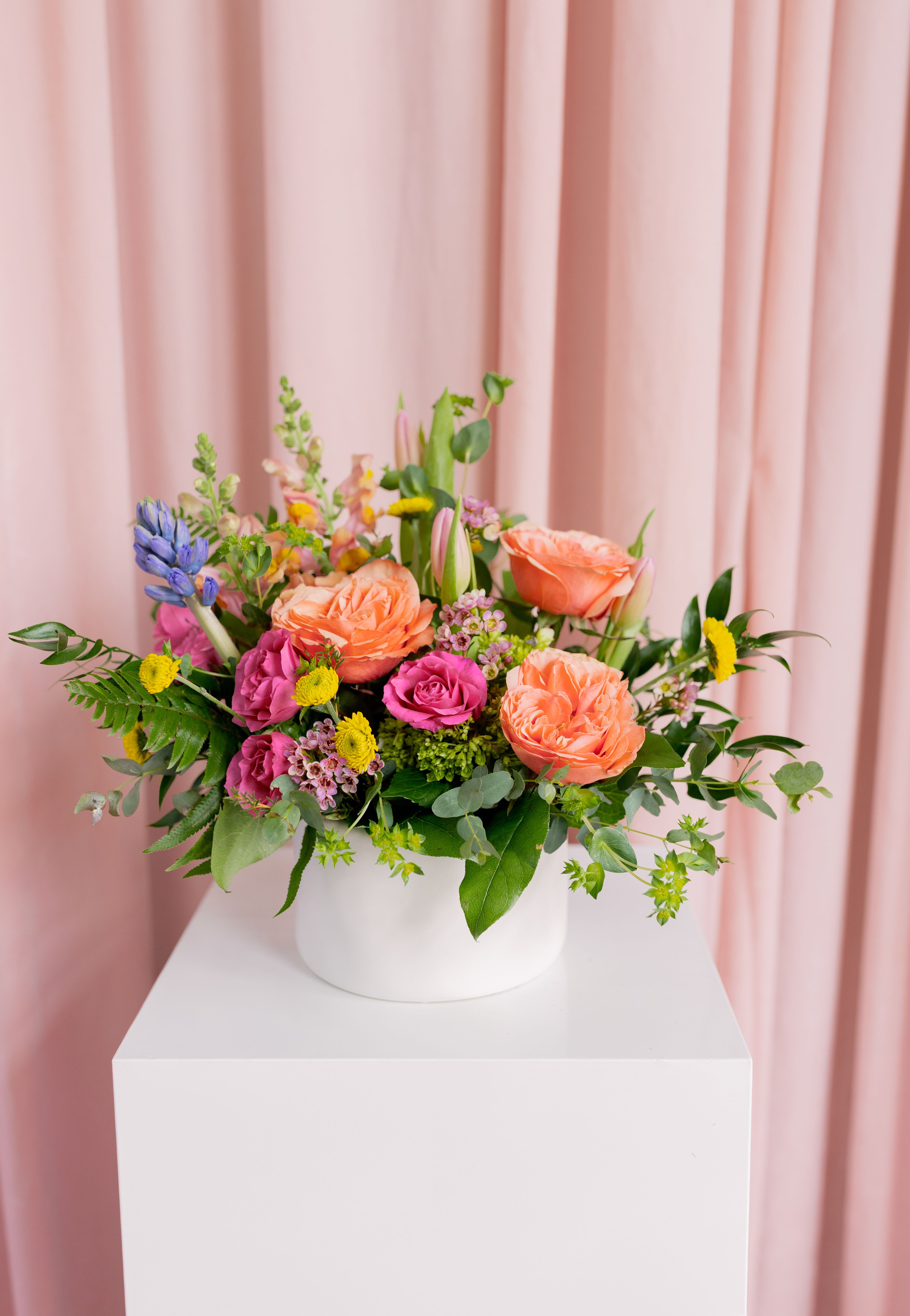 Mixed bouquet of peach, pink, and yellow flowers in a white vase