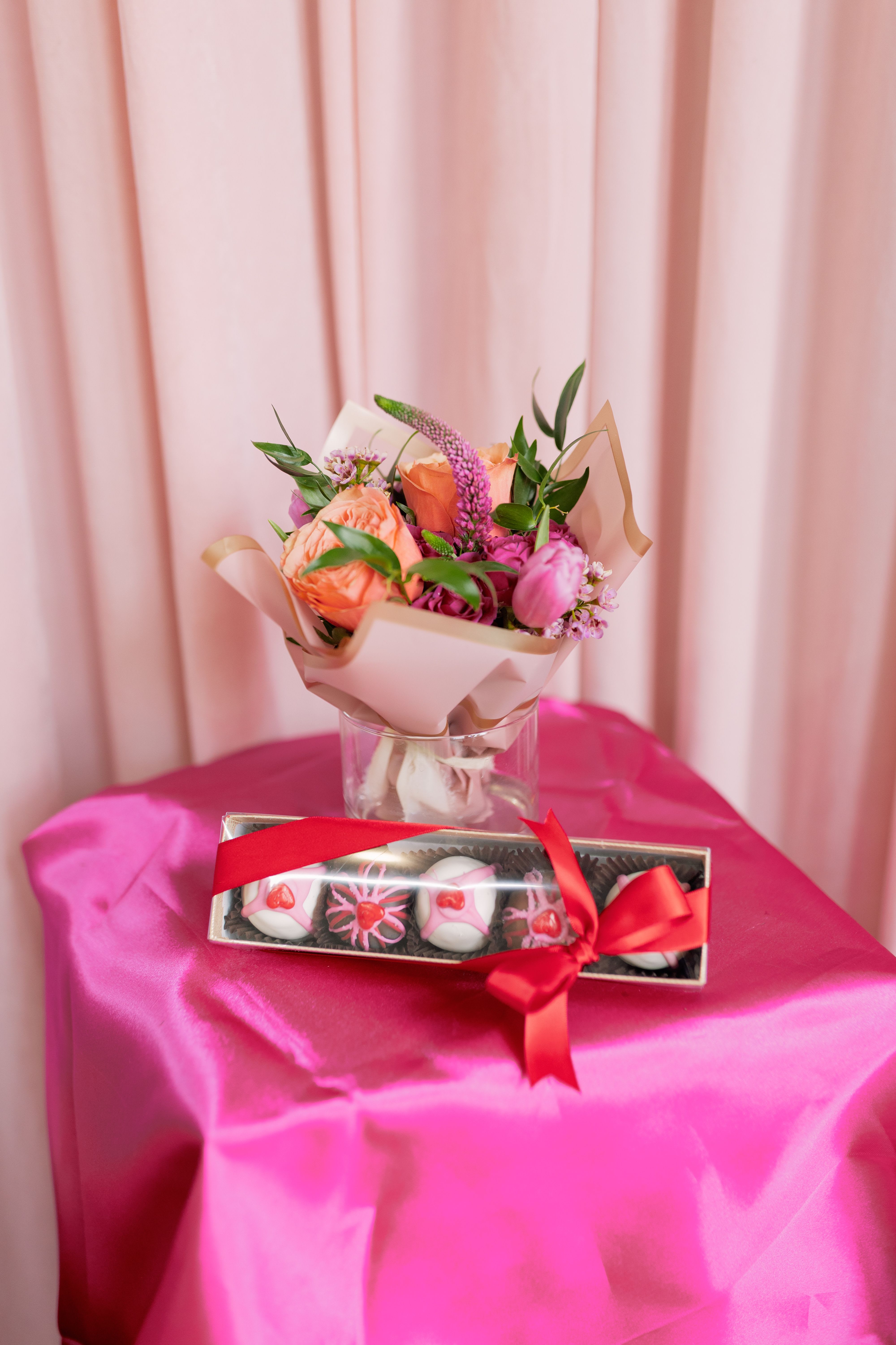 Pink and peach bouquet in a glass vase with a box of chocolates