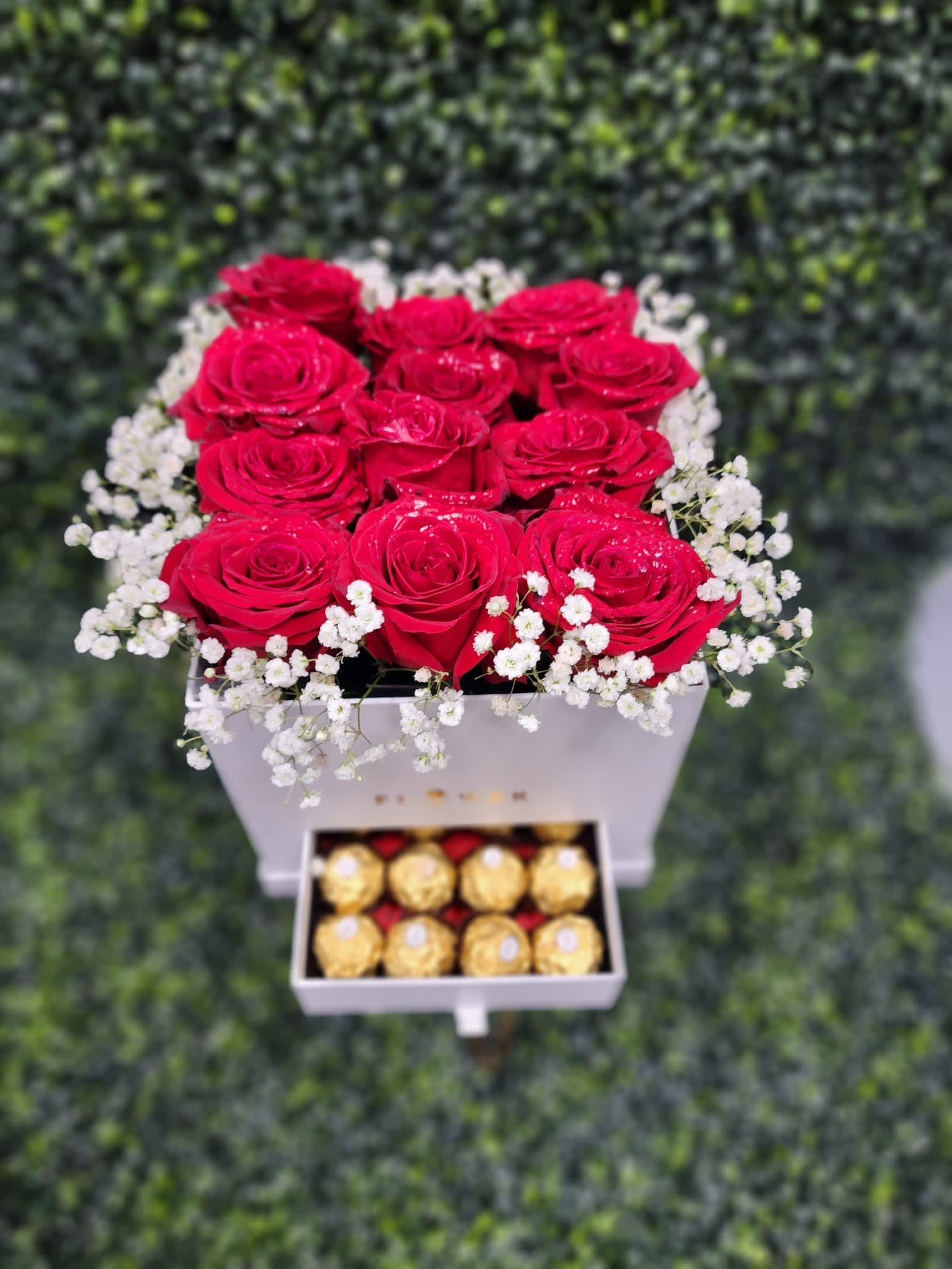 Red roses in a white box with baby’s breath and chocolates below