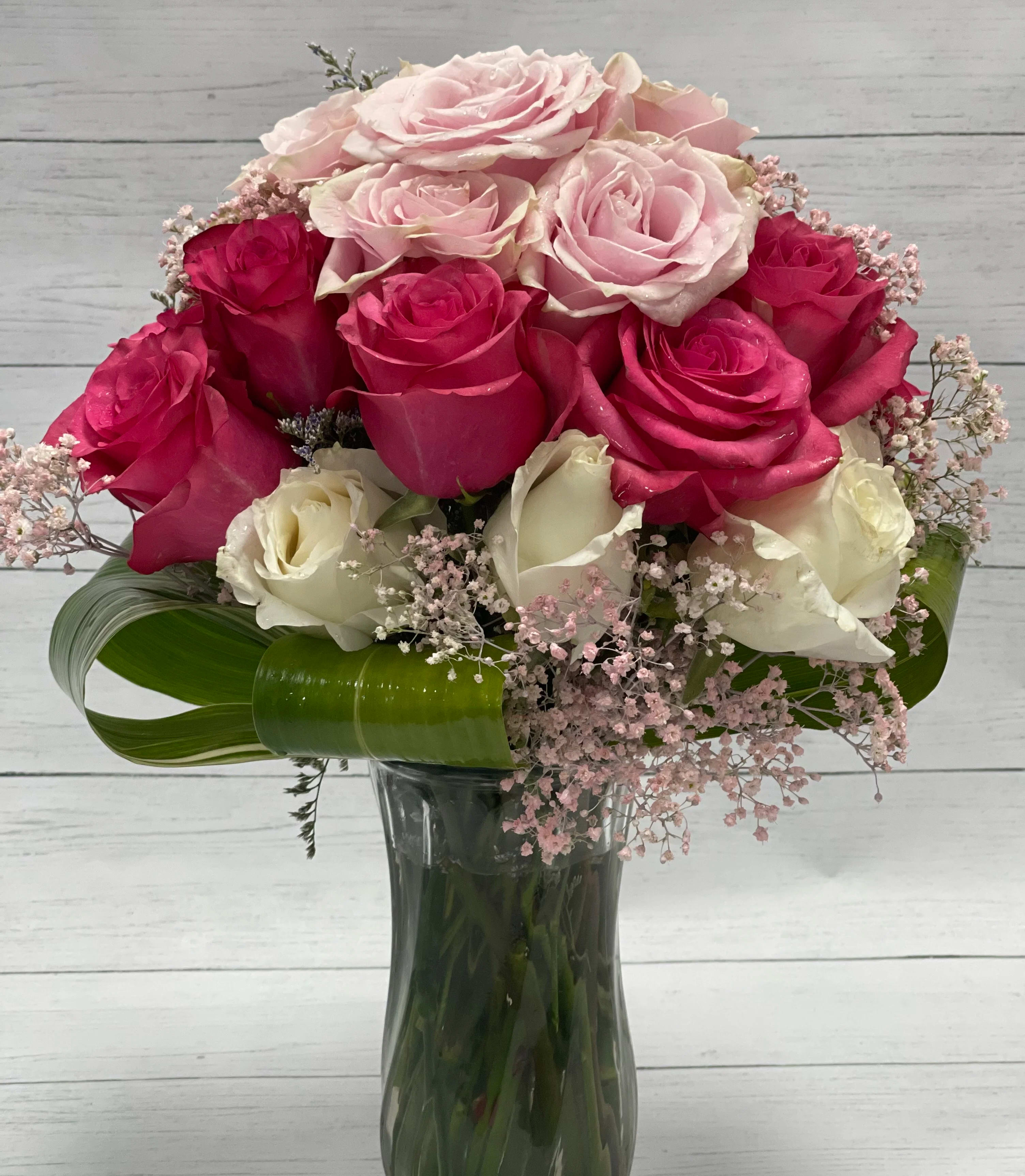 Pink and white roses arranged in a glass vase with pink filler flowers