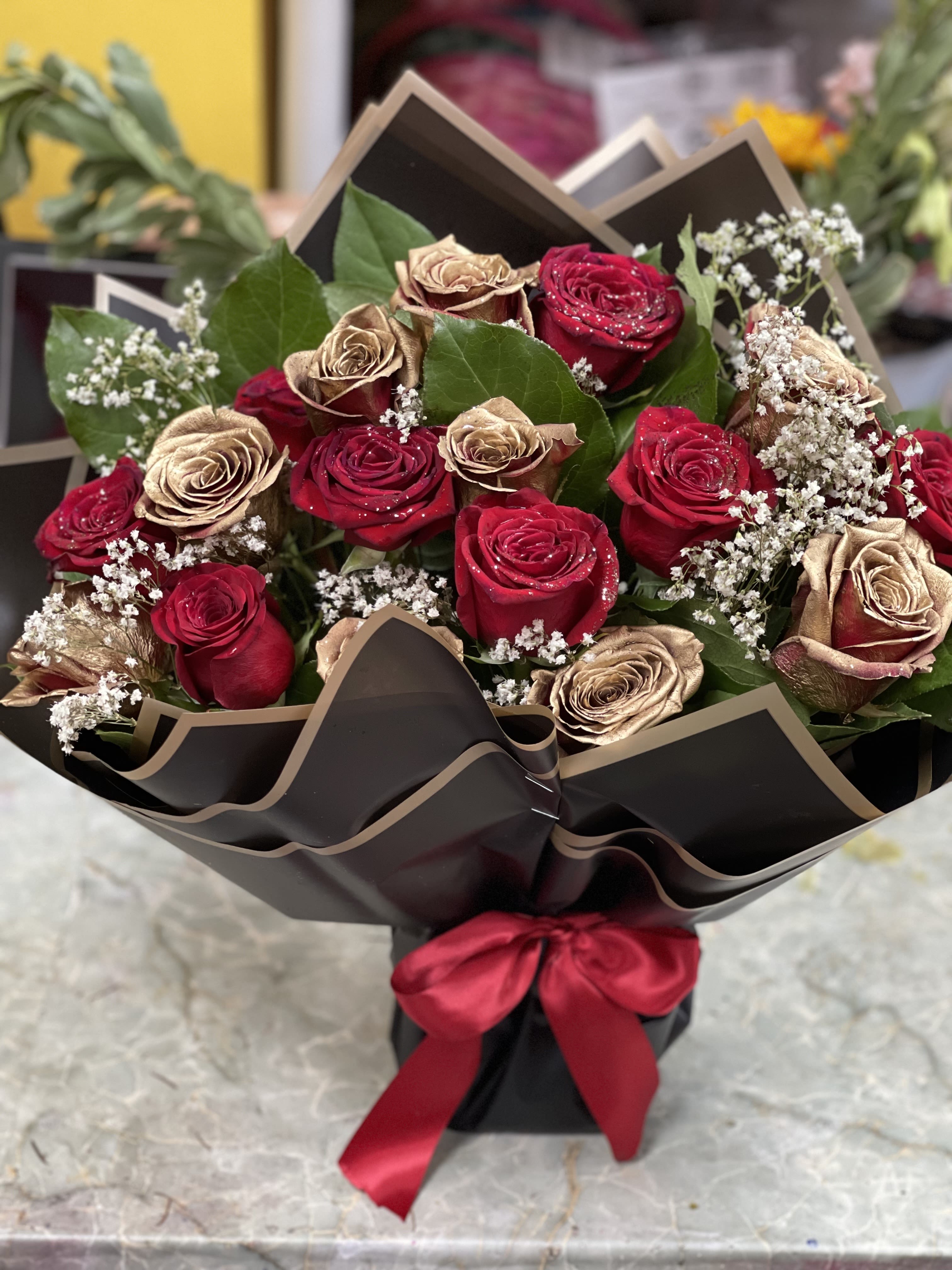 Bouquet of red and gold roses wrapped in black paper with a red ribbon