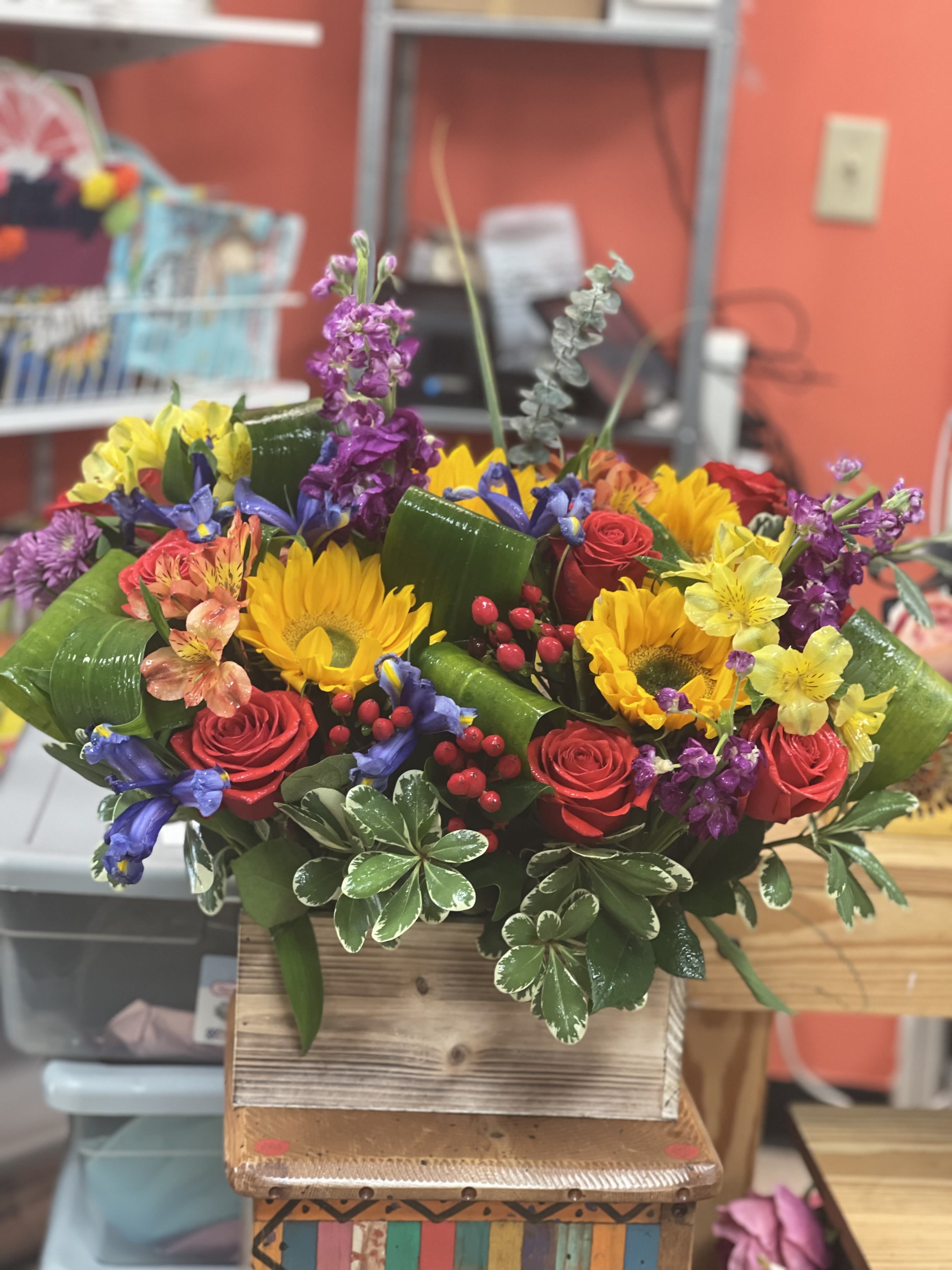 Colorful mixed bouquet with roses, sunflowers, and purple blooms in a wooden box