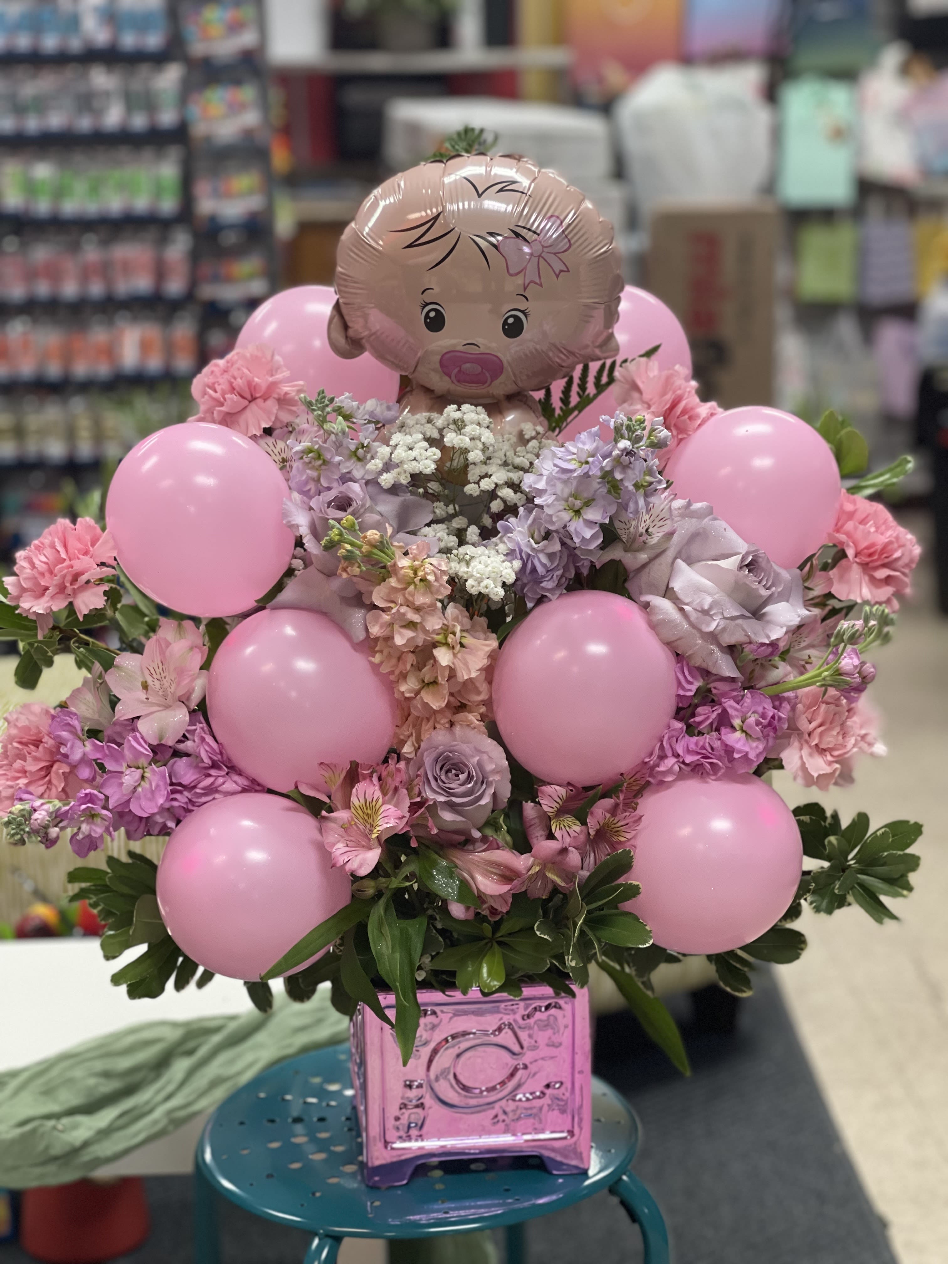 Cherishable Charm  - Welcome a little bundle of joy with our charming cherishable charm bouquet — a soft and whimsical arrangement perfect for celebrating new beginnings. Featuring delicate lavender roses, fluffy pink carnations, and playful pink balloons, this bouquet is topped with an adorable baby-themed balloon for a joyful touch. The gentle blend of pink and lavender tones creates a sweet, soothing palette that’s ideal for baby showers, gender reveals, or welcoming a newborn. Beautifully arranged with love, Sweet Baby Bloom is a heartfelt way to share in the happiness of new life.