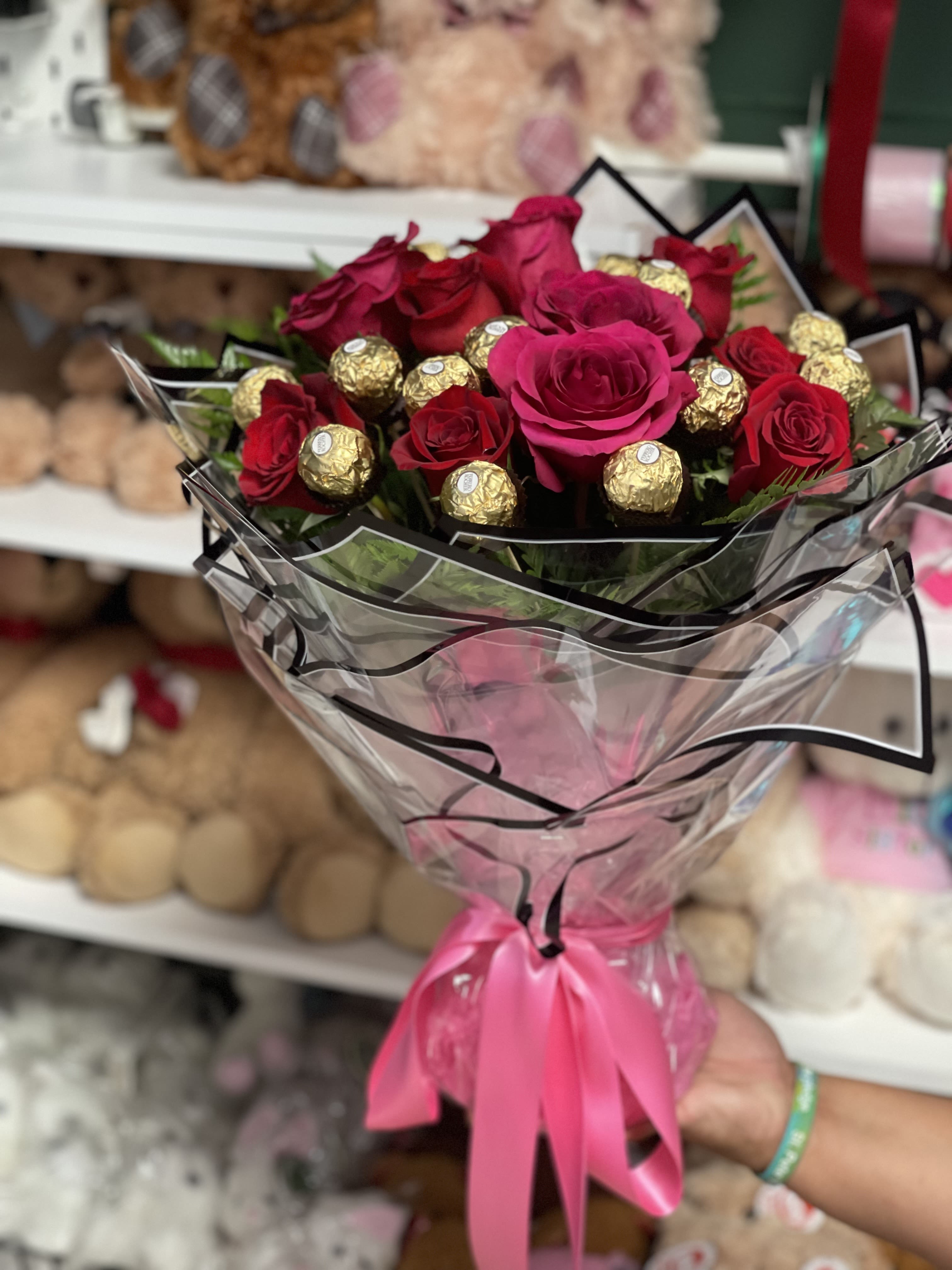 Bouquet of red roses and gold-wrapped chocolates in clear wrap with a pink ribbon