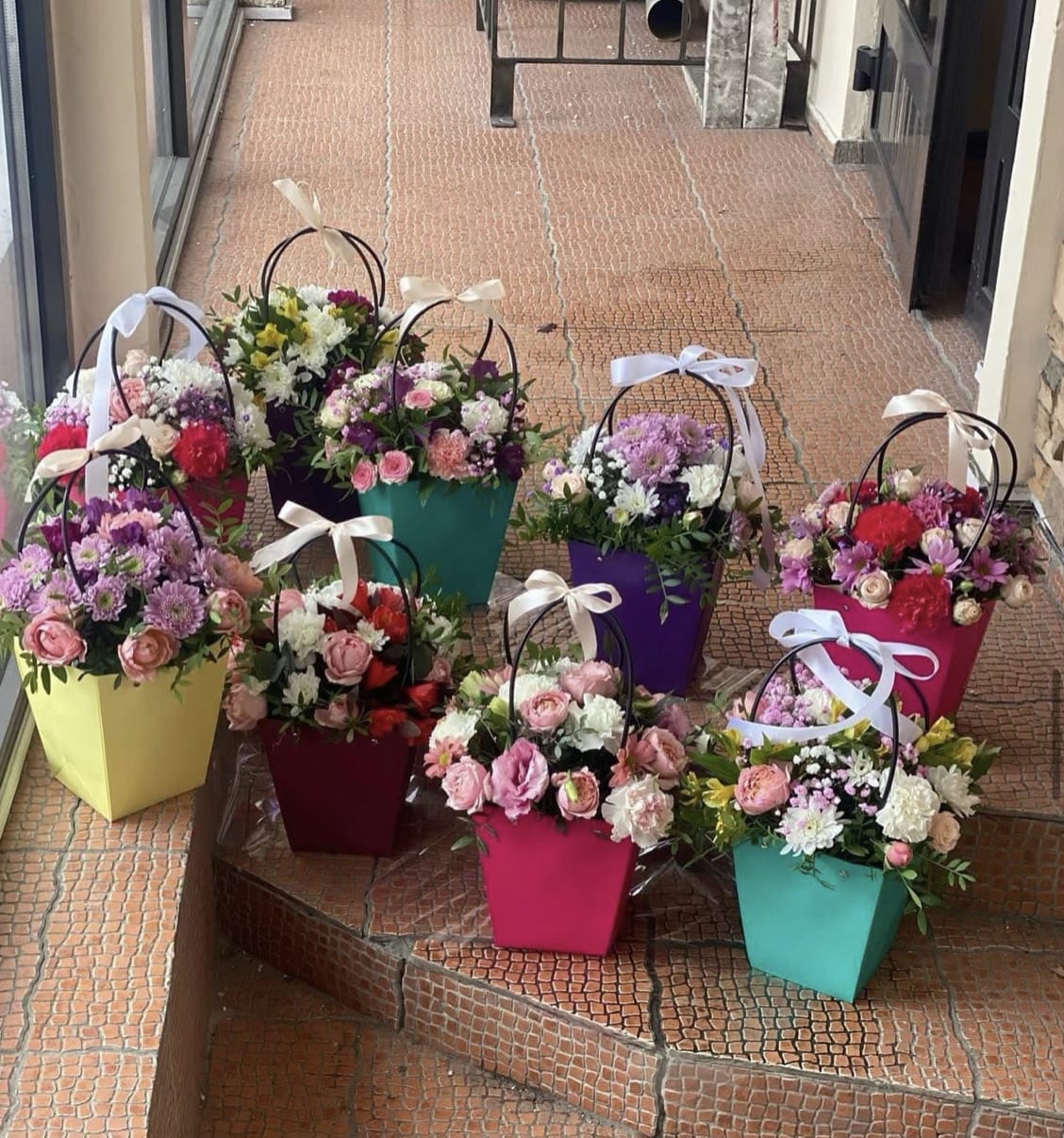 Colorful flower baskets with mixed blooms and ribbon handles arranged on steps