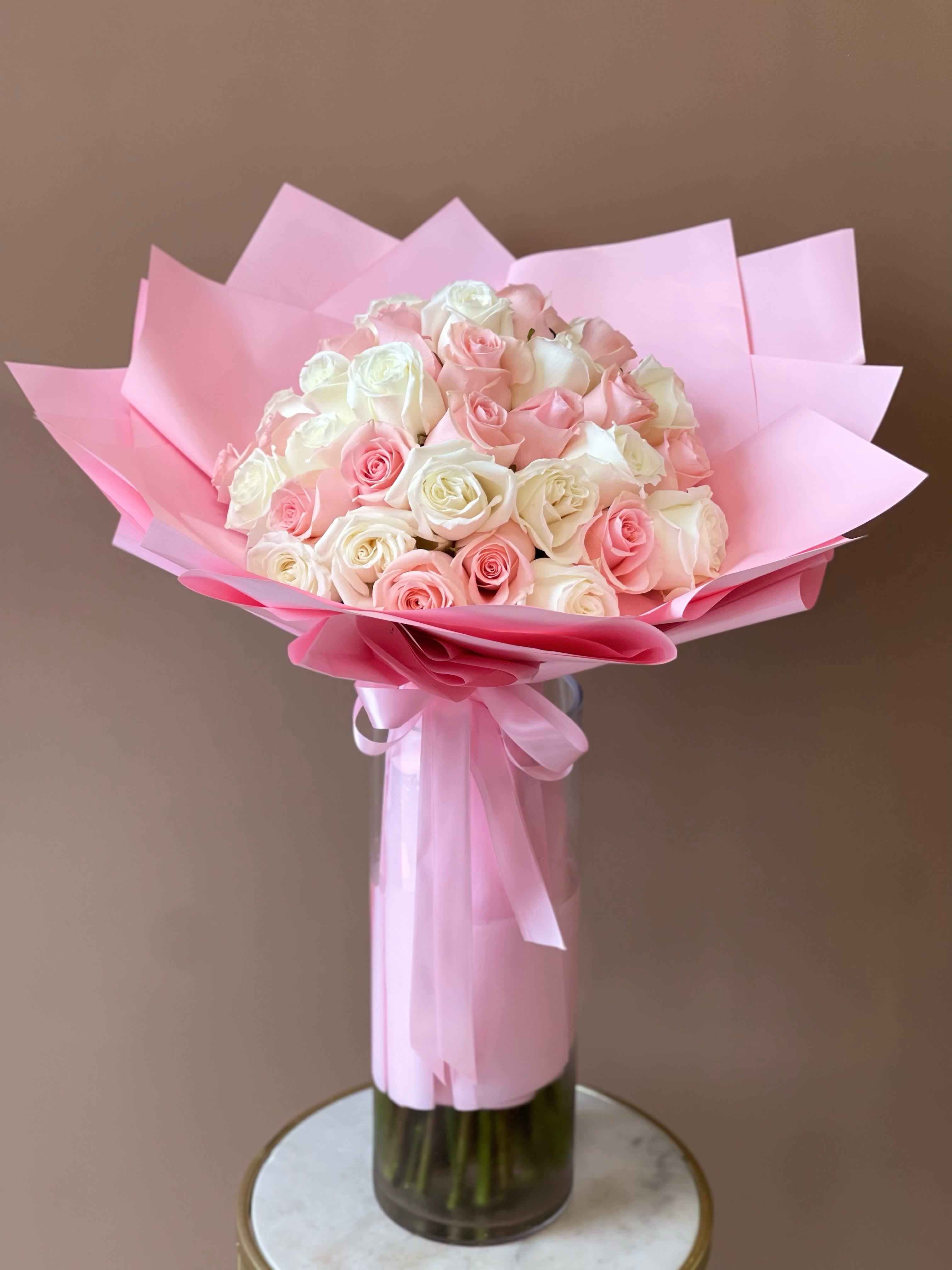 Bouquet of pink and white roses wrapped in pink paper in a glass vase