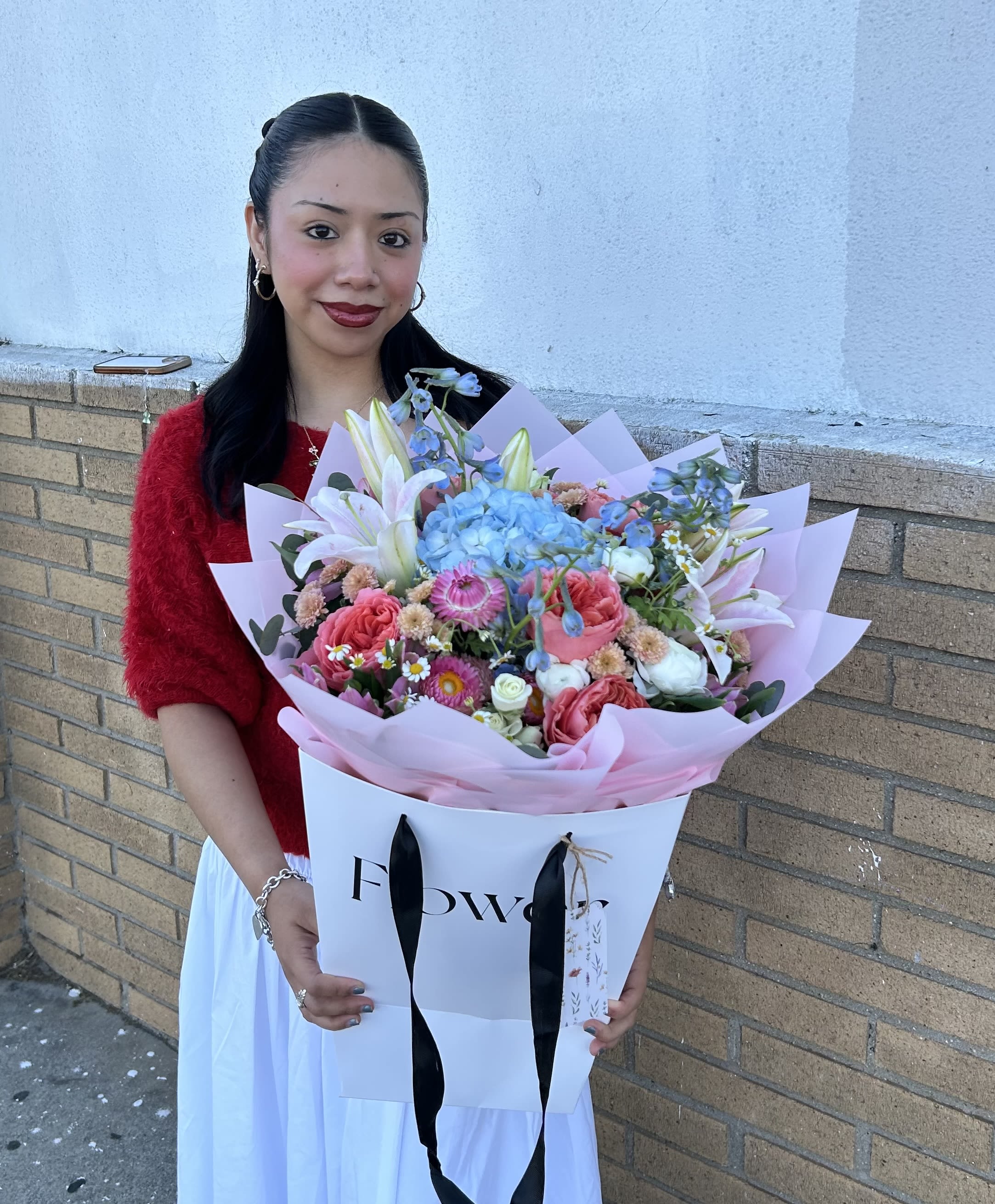Woman holding a large pastel bouquet with lilies, roses, and blue hydrangeas