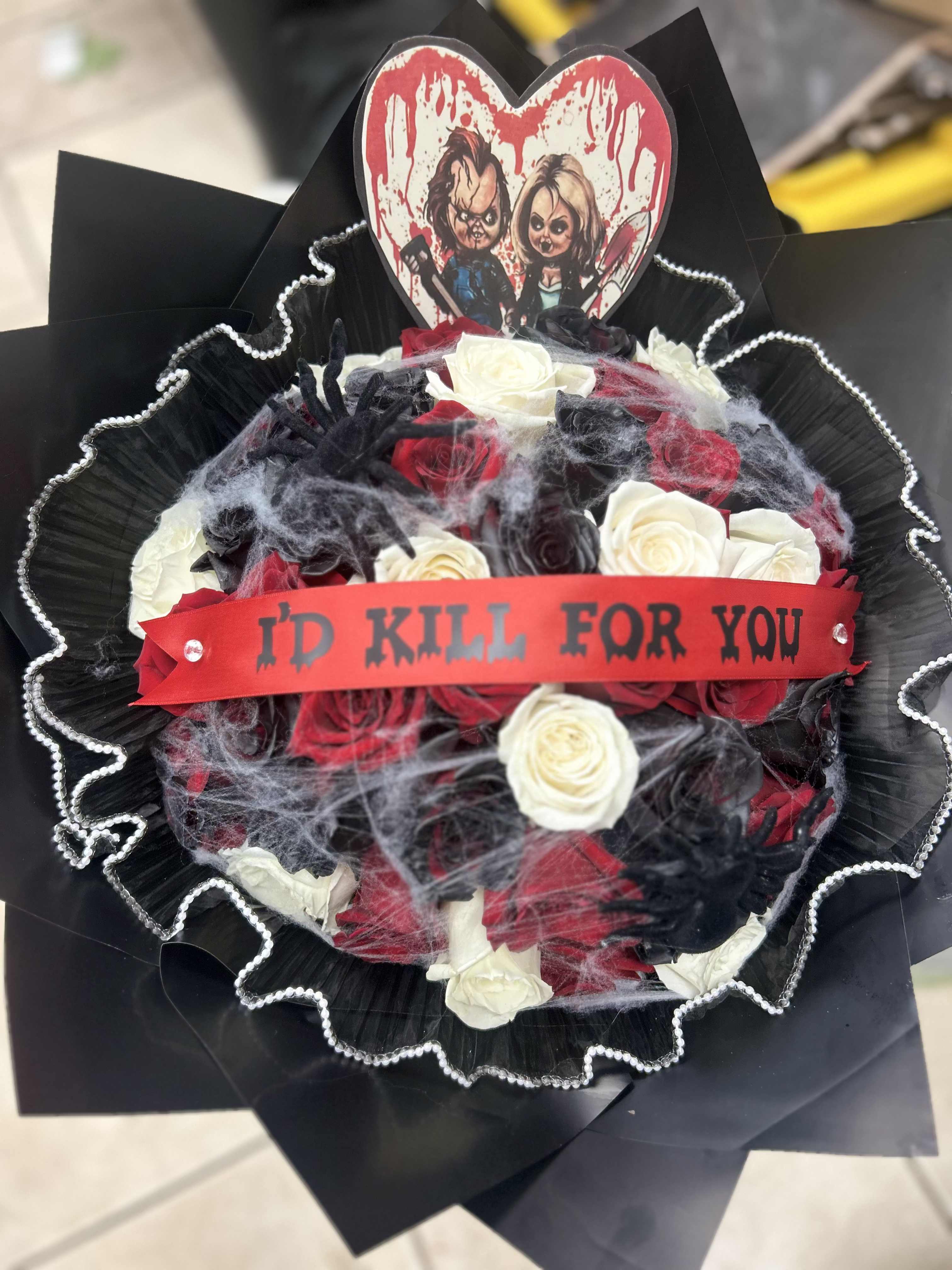 Black-wrapped bouquet of red, white, and black roses with a horror-themed topper