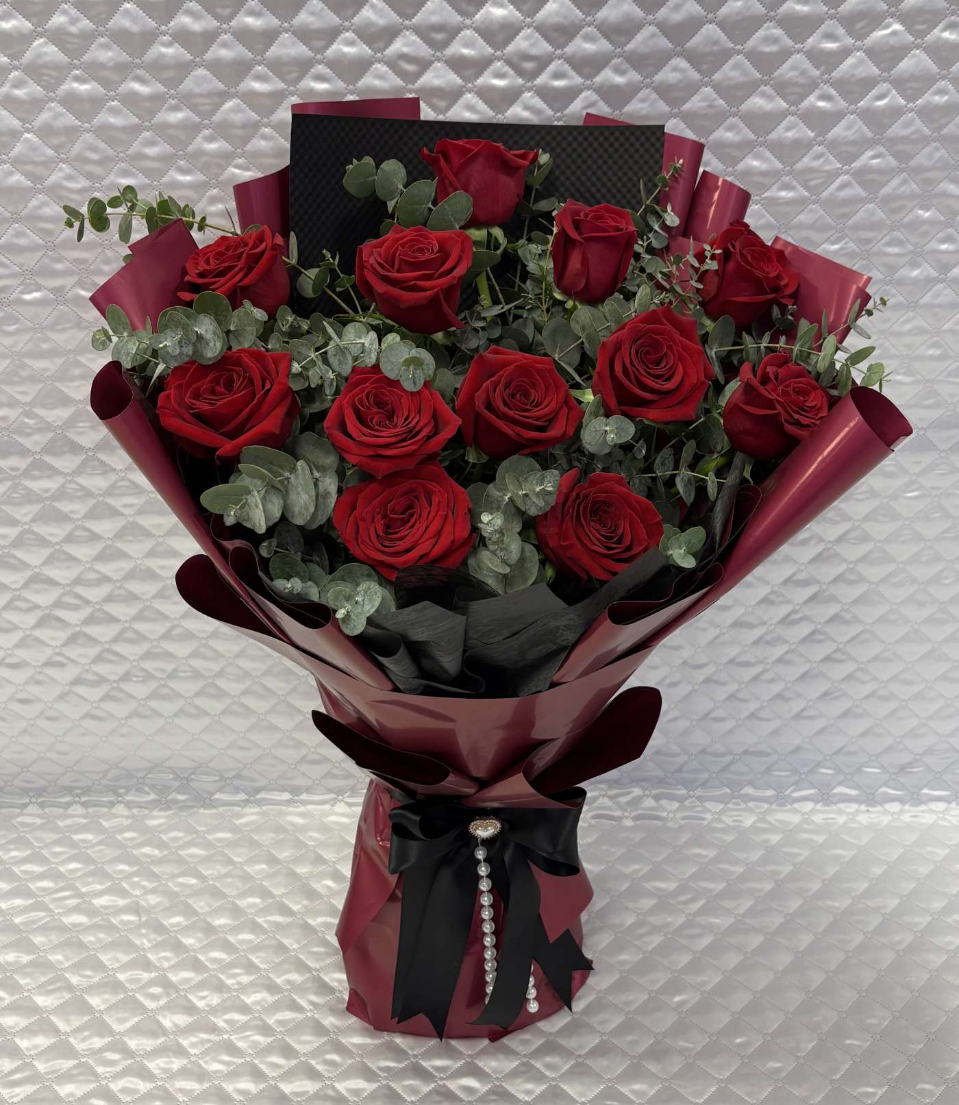 Bouquet of red roses wrapped in burgundy paper with a black ribbon