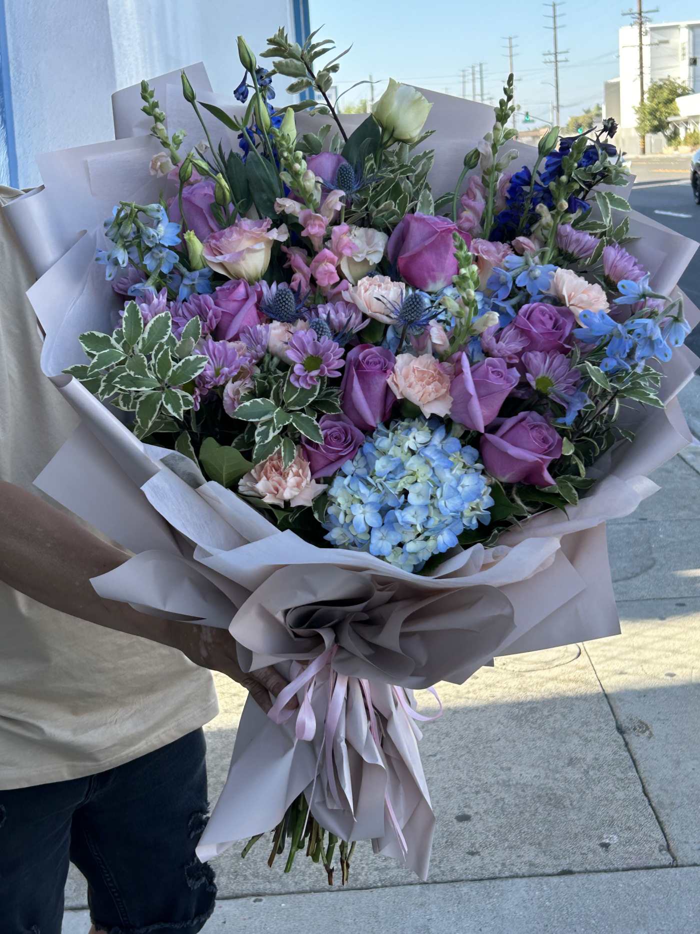 Large bouquet of purple, blue, and pink flowers wrapped in pale paper