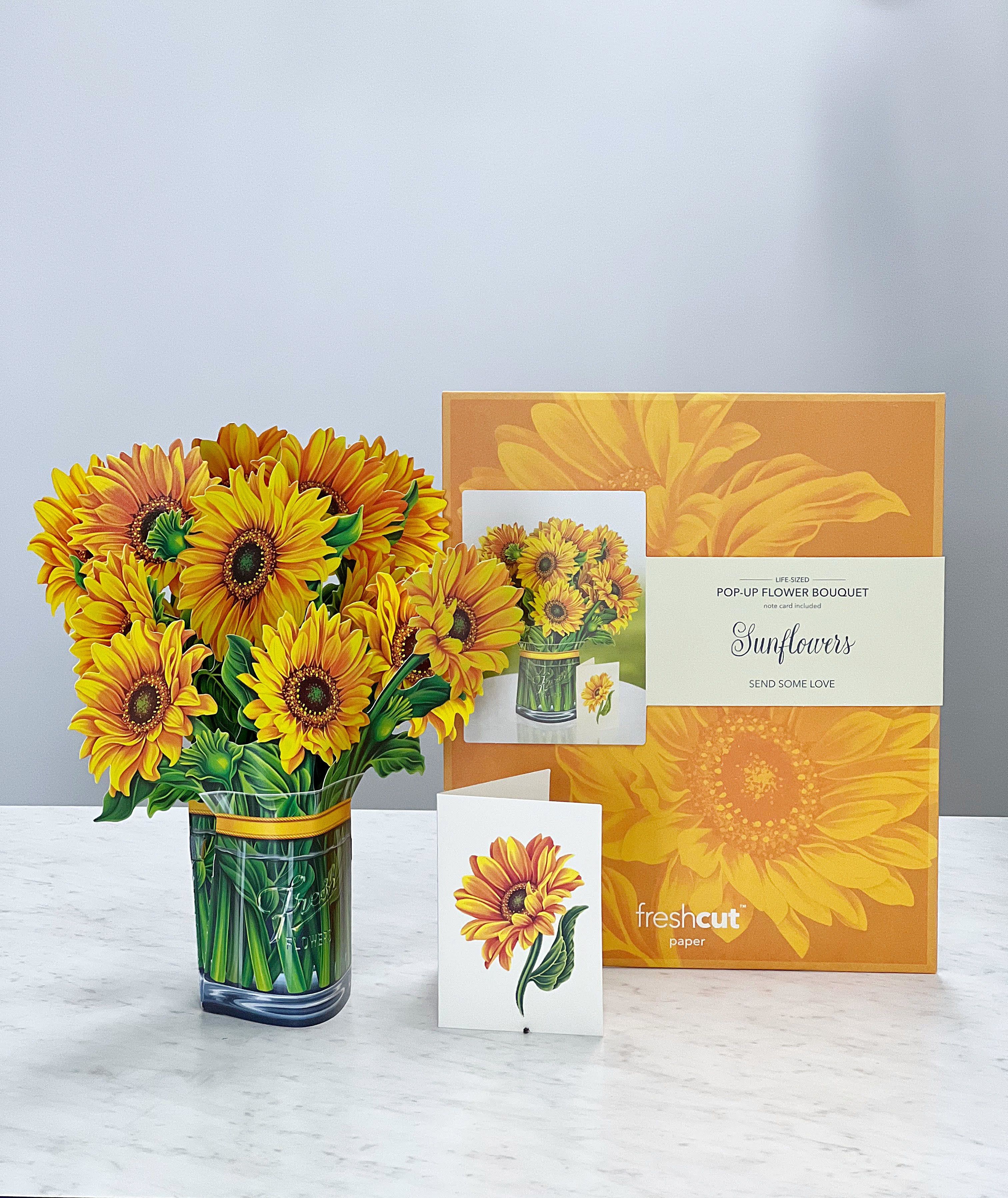 Pop-up bouquet of yellow sunflowers in a glass vase with an orange gift box