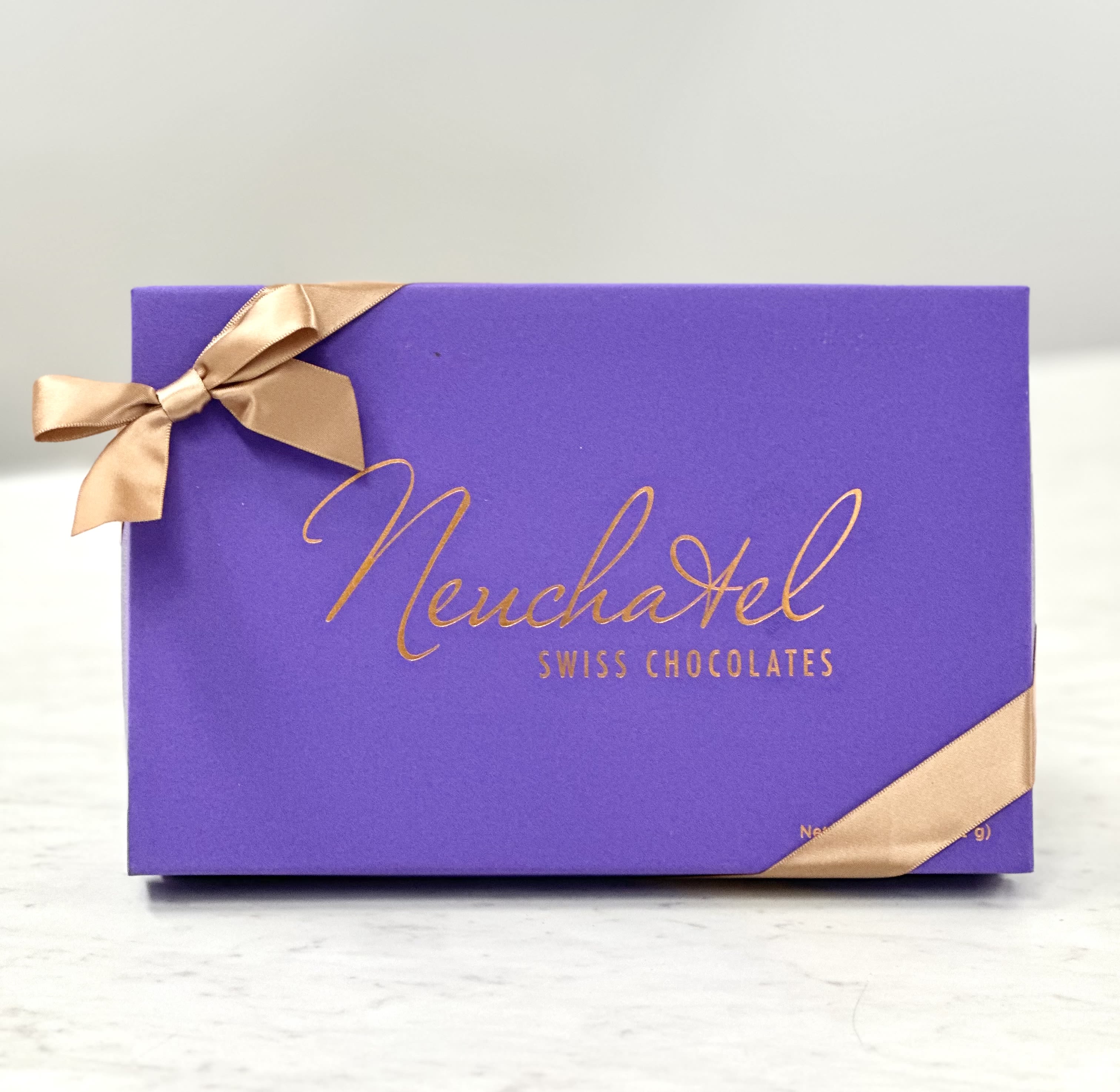 Purple box of Neuchatel Swiss chocolates tied with gold ribbon