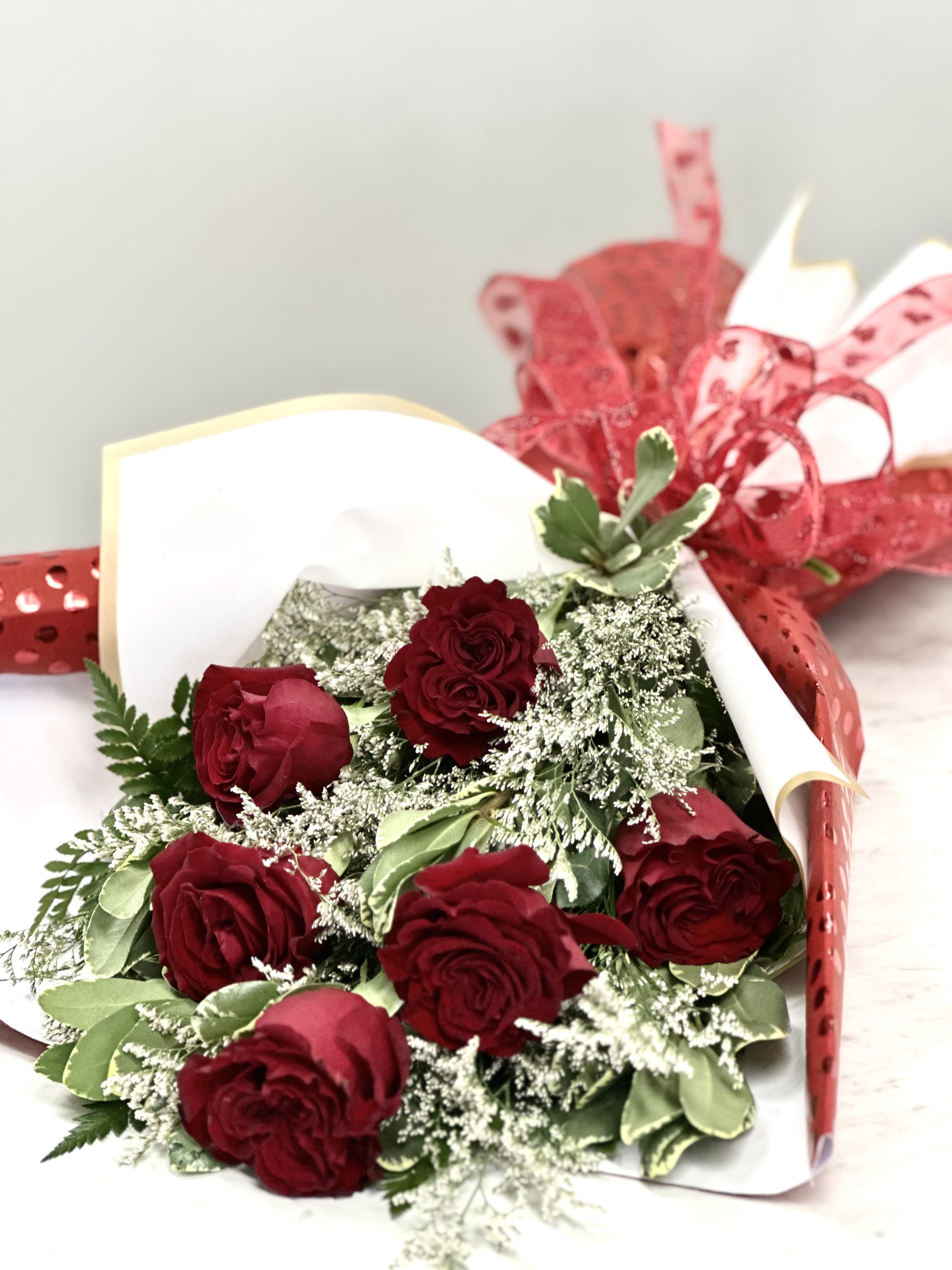 Bouquet of red roses wrapped in white paper with red ribbon