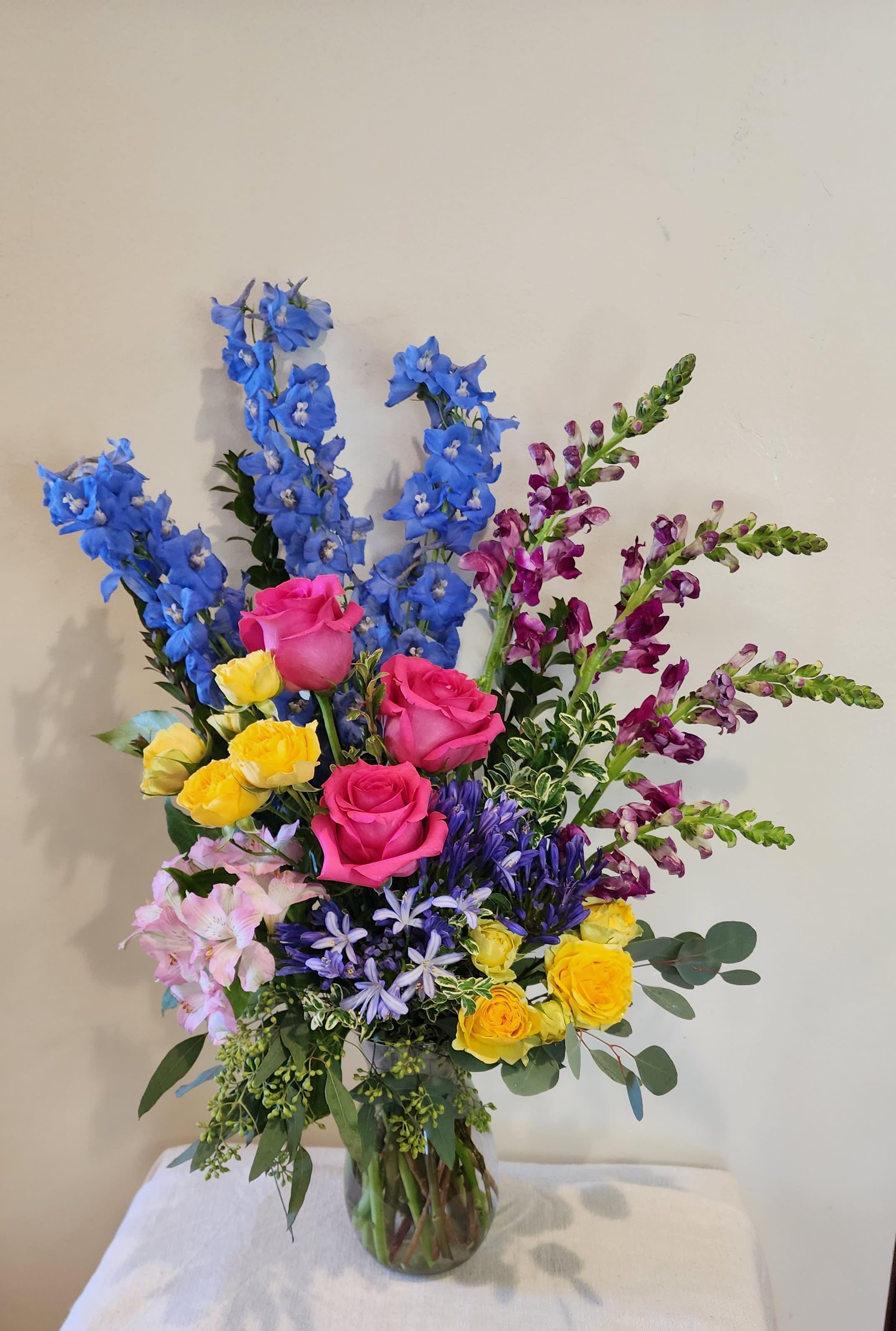 Colorful mixed bouquet in a clear glass vase with tall blue and purple blooms
