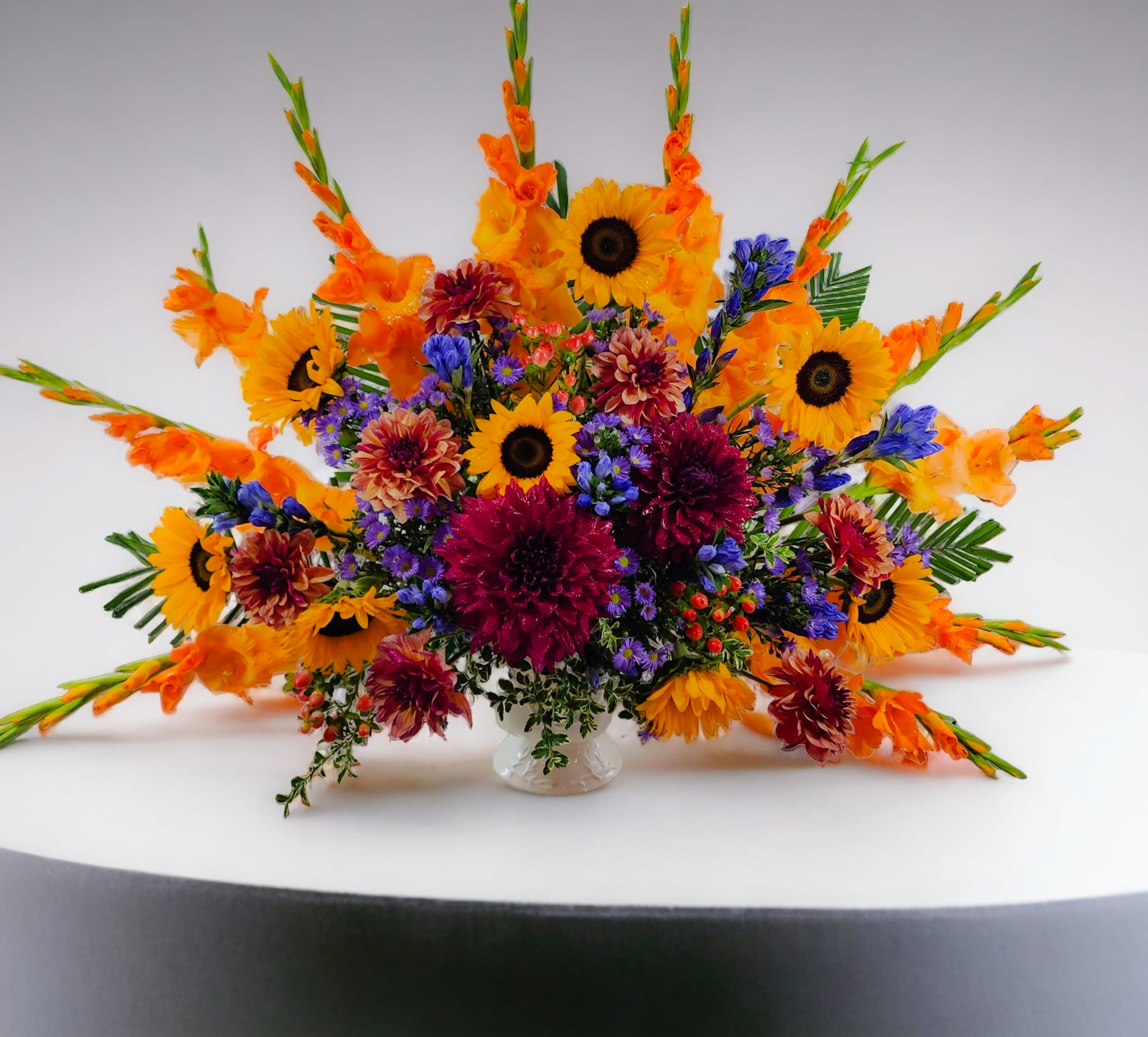 Bright mixed bouquet with sunflowers, orange gladiolus, and purple blooms in a clear vase