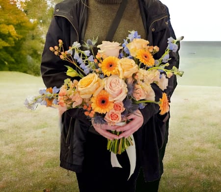 Person holding a bouquet of peach, pink, and orange flowers