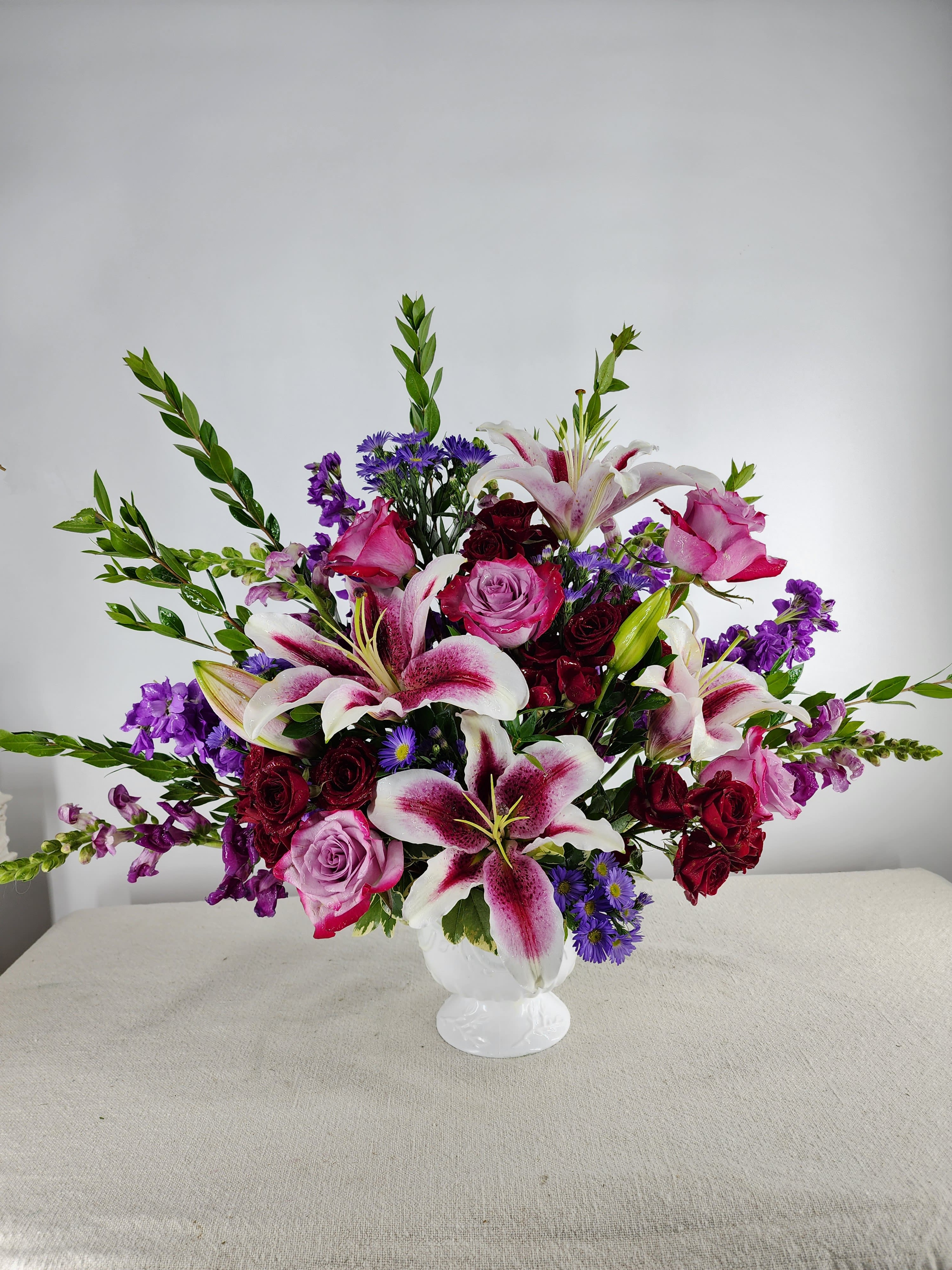 Mixed bouquet of pink roses, lilies, and purple flowers in a white vase